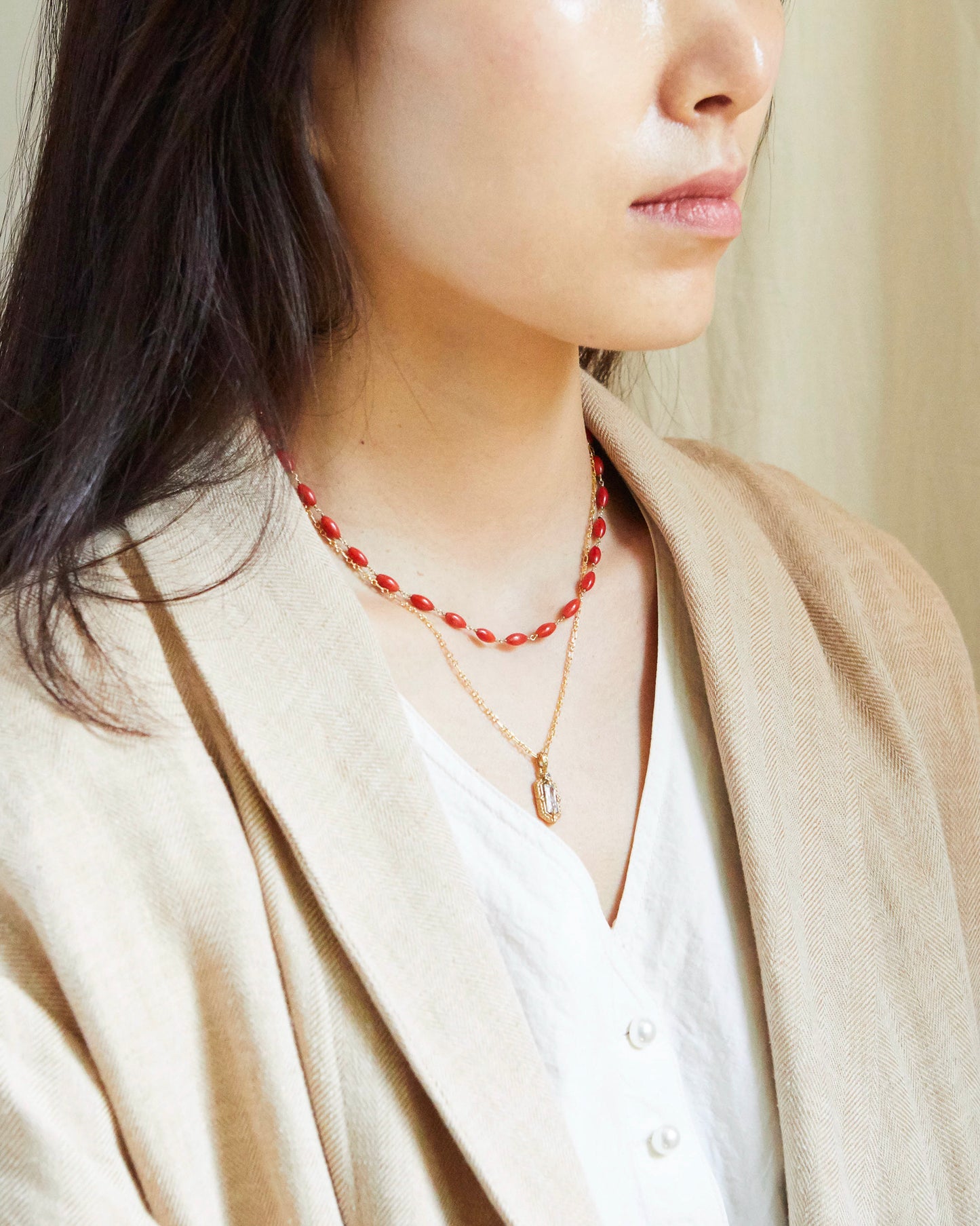 Person wearing a red beaded necklace and a beige cardigan.