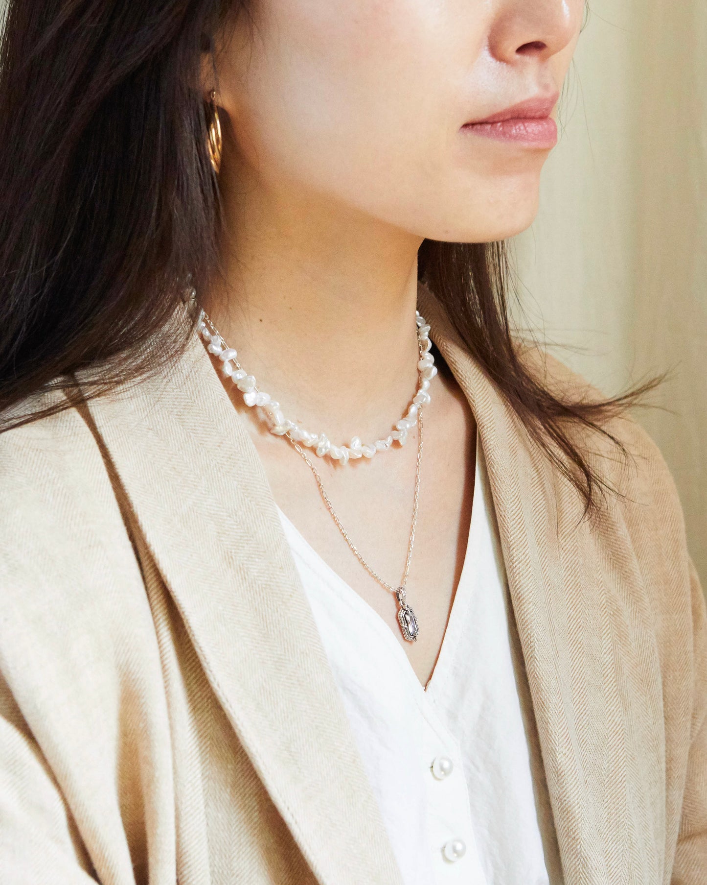 Close-up of a person wearing pearl necklaces and a beige blazer.