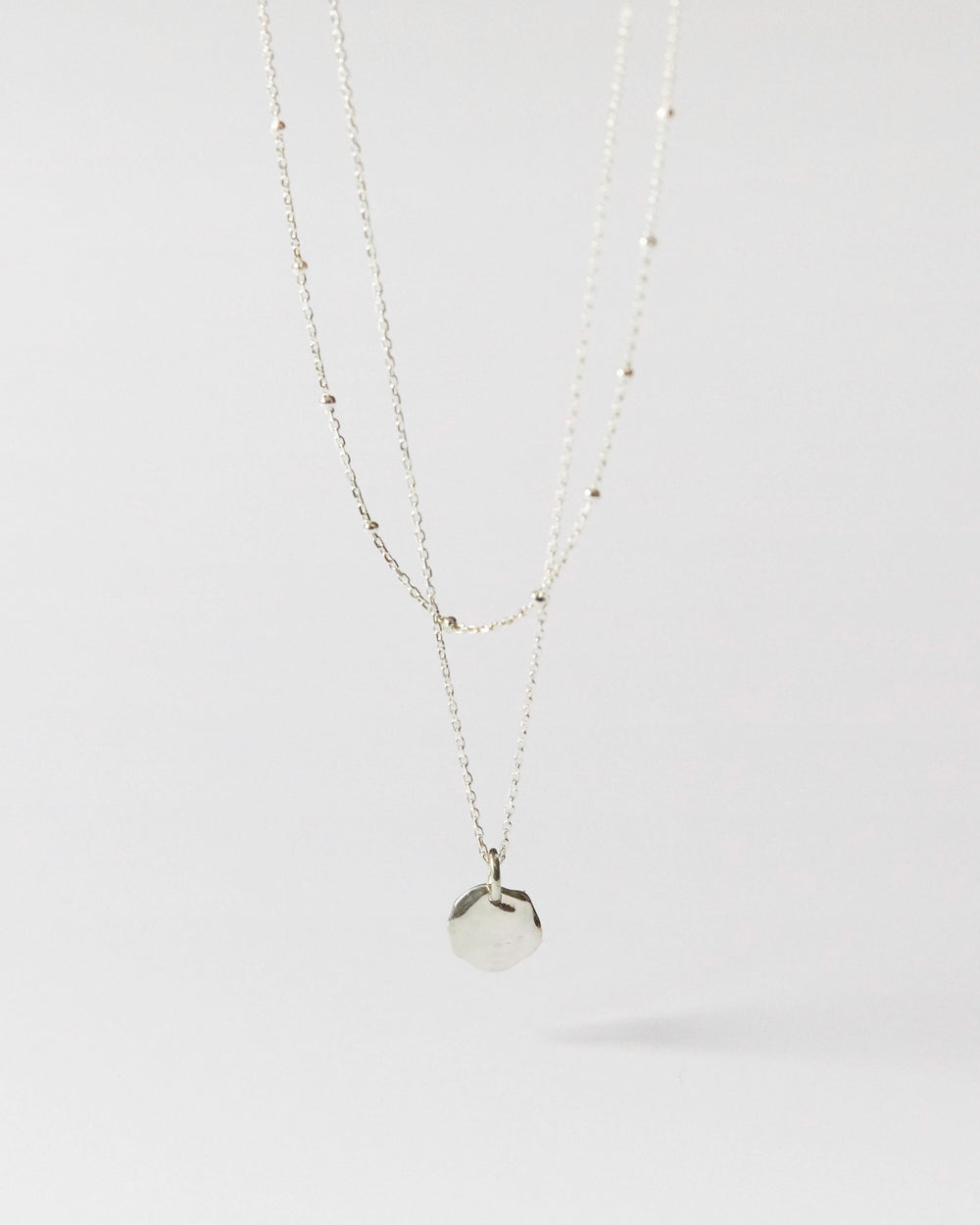 Flat lay of minimalist silver pendant necklace with delicate bead-accented chain