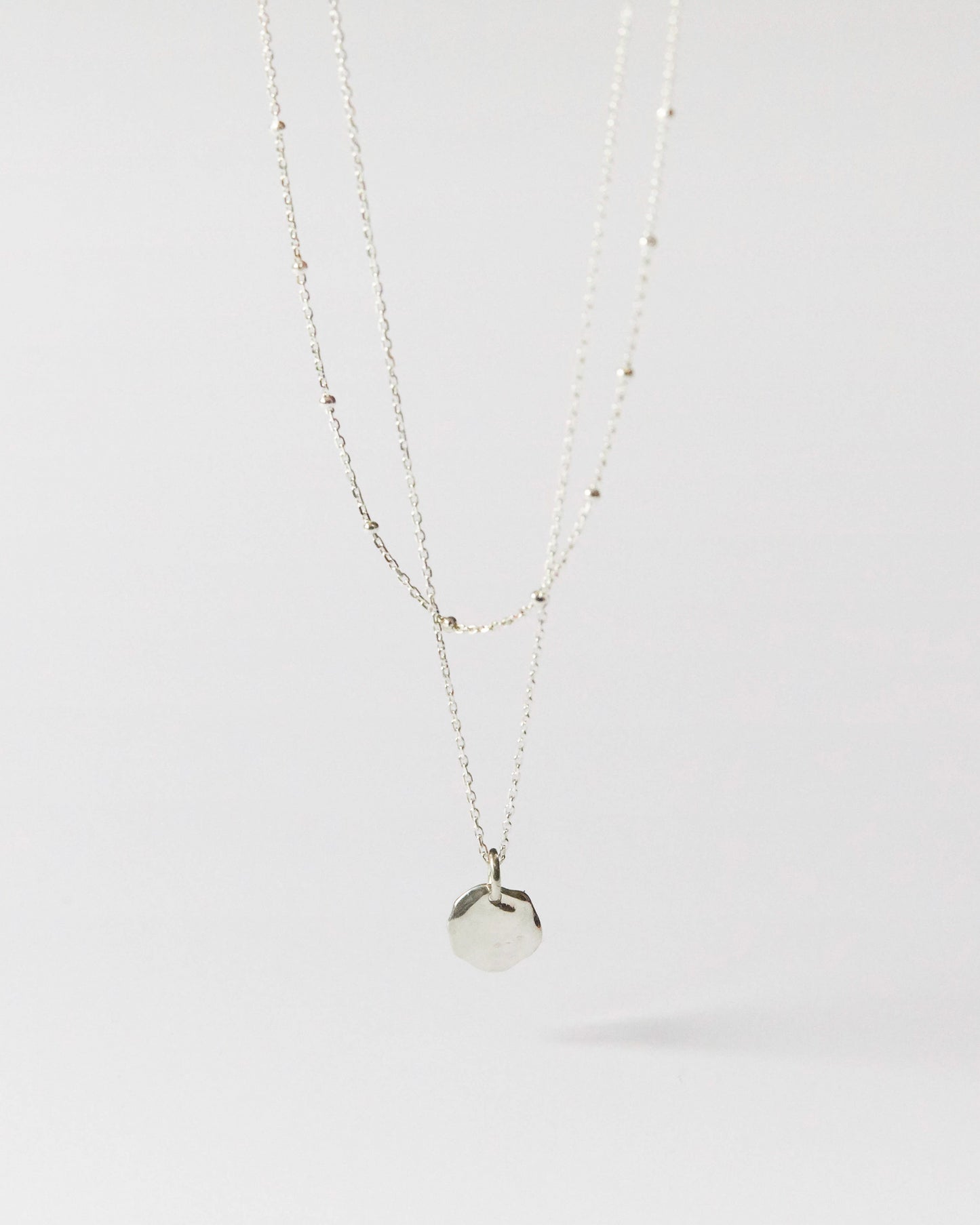 Flat lay of minimalist silver pendant necklace with delicate bead-accented chain