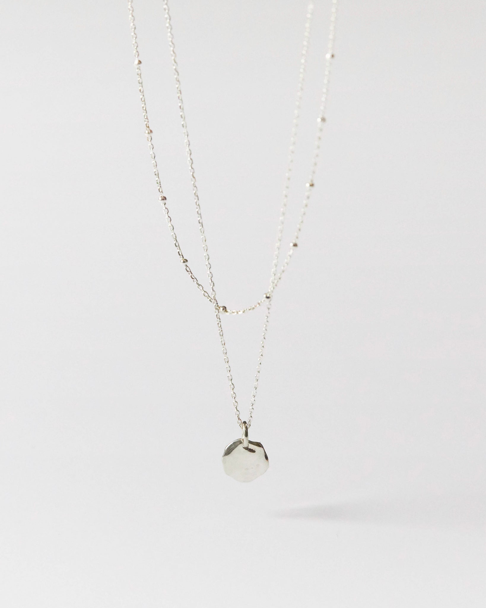 Flat lay of minimalist silver pendant necklace with delicate bead-accented chain