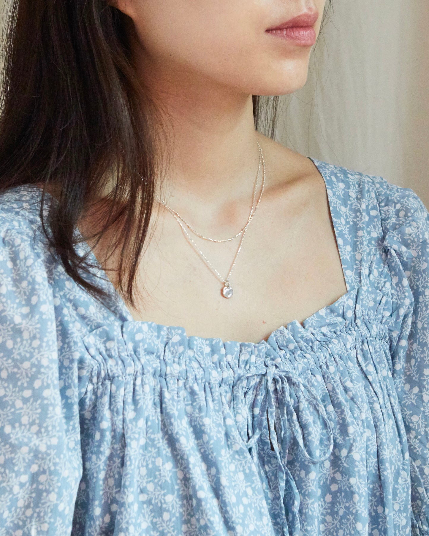 Close-up of a person wearing a light blue floral dress with a delicate necklace.