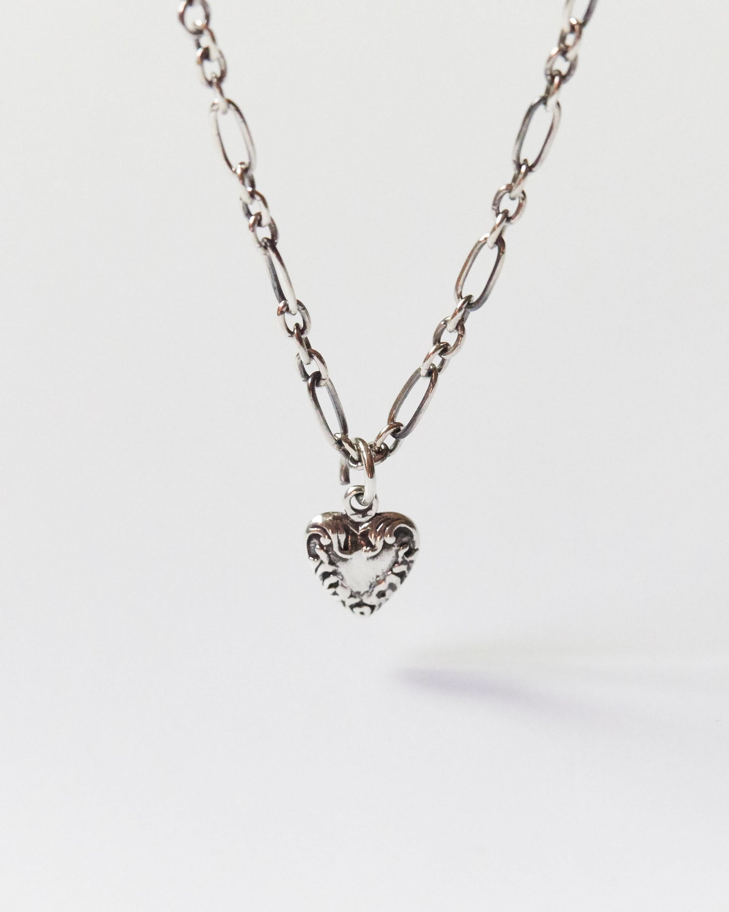 Close-up of a silver heart pendant necklace with mixed chain on skin