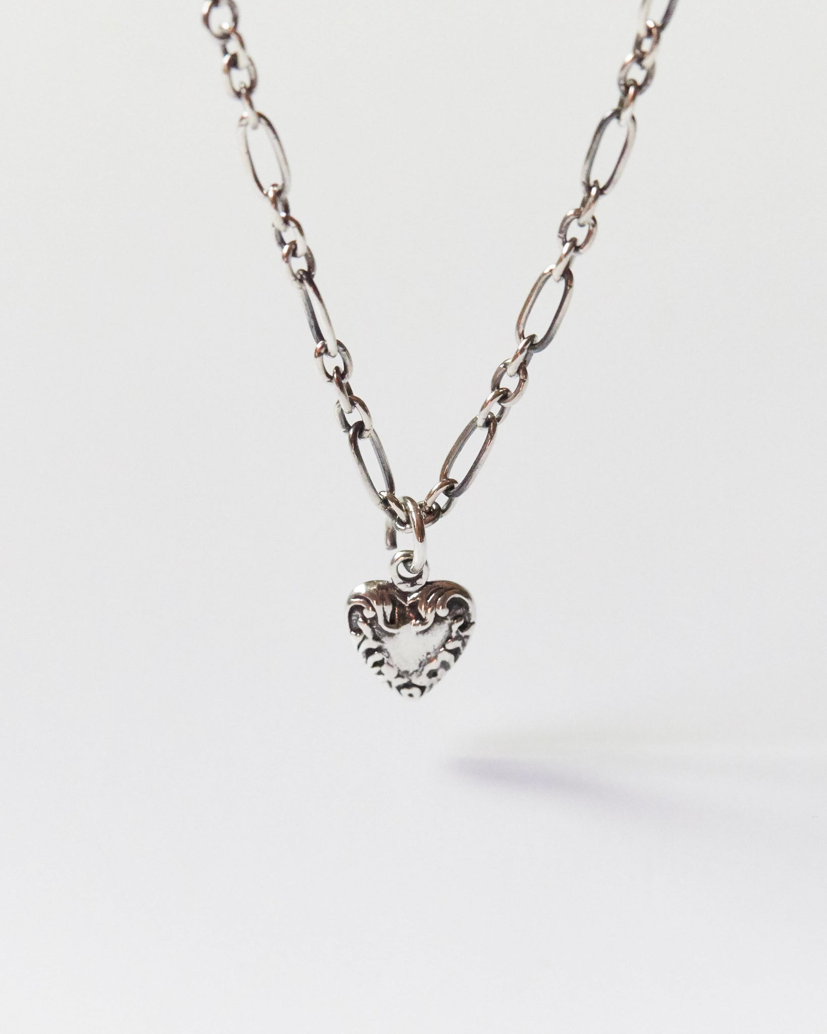 Close-up of a silver heart pendant necklace with mixed chain on skin