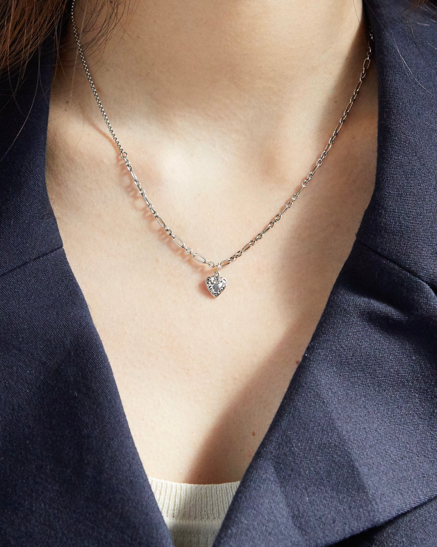 Silver heart charm necklace styled over navy blazer and cream top