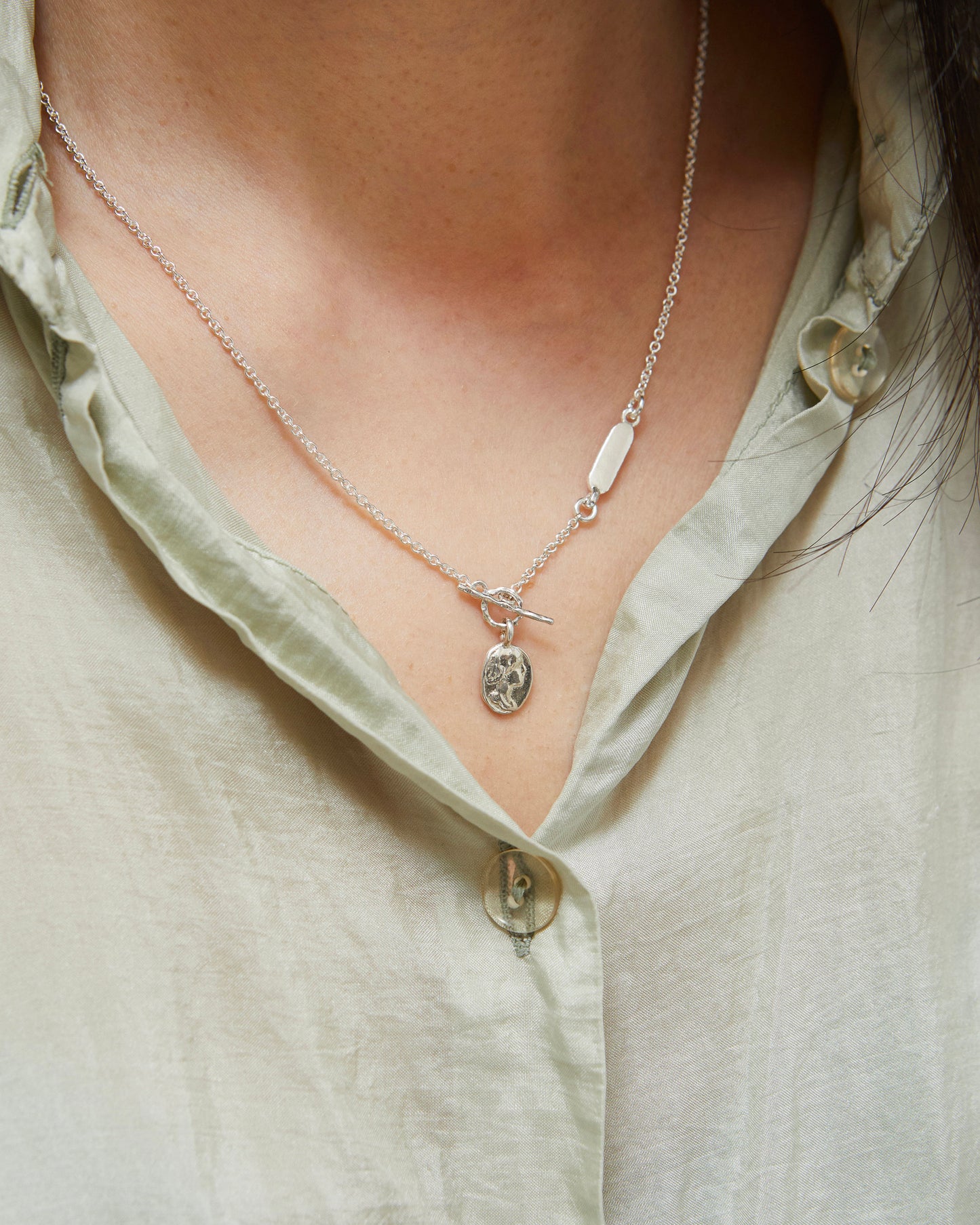 Silver necklace with a pendant on a person wearing a light green shirt