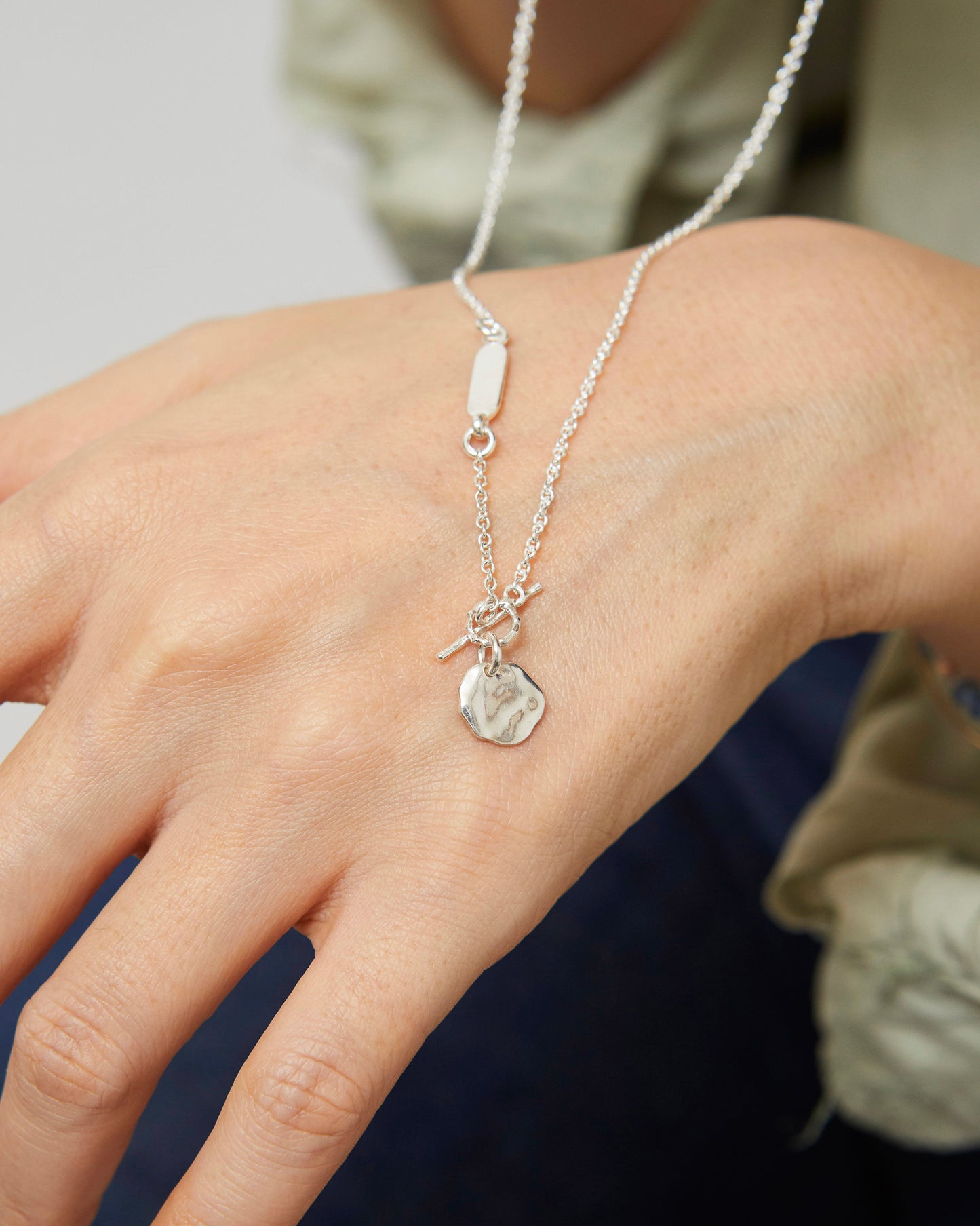 Close-up of silver pendant necklace styled with casual outfit