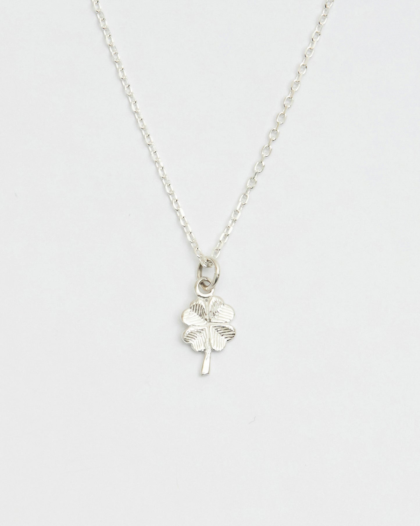 Minimal silver four leaf clover necklace displayed on white background