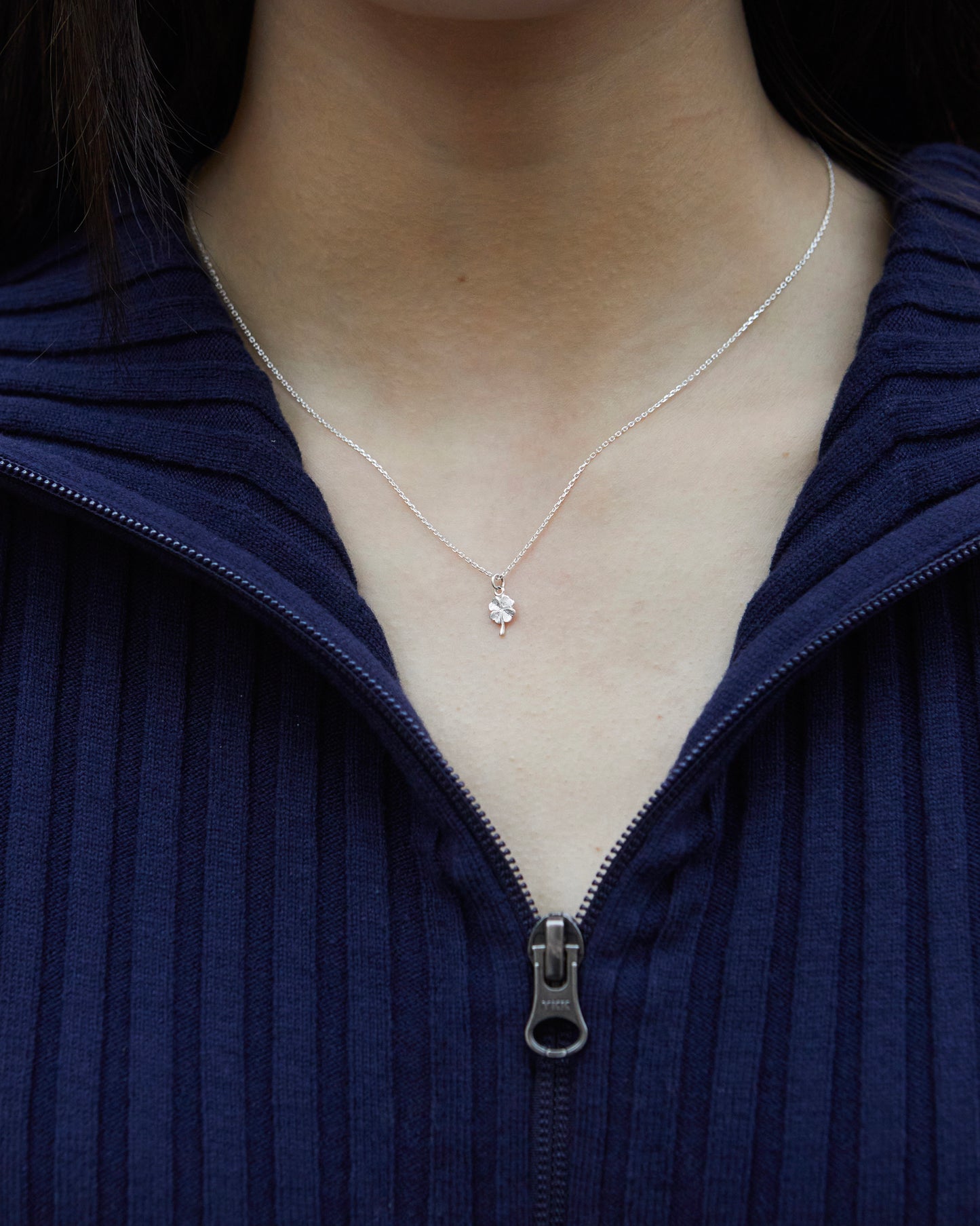 Minimal silver four leaf clover necklace centered on neckline for everyday styling