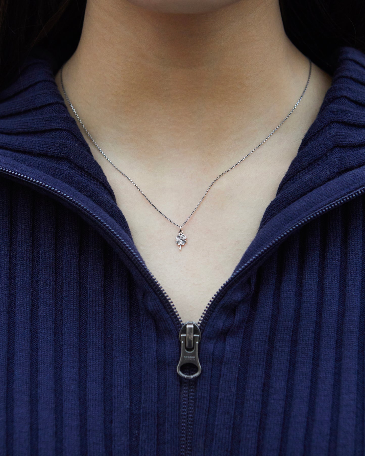 Minimal silver four leaf clover necklace centered on neckline for everyday styling