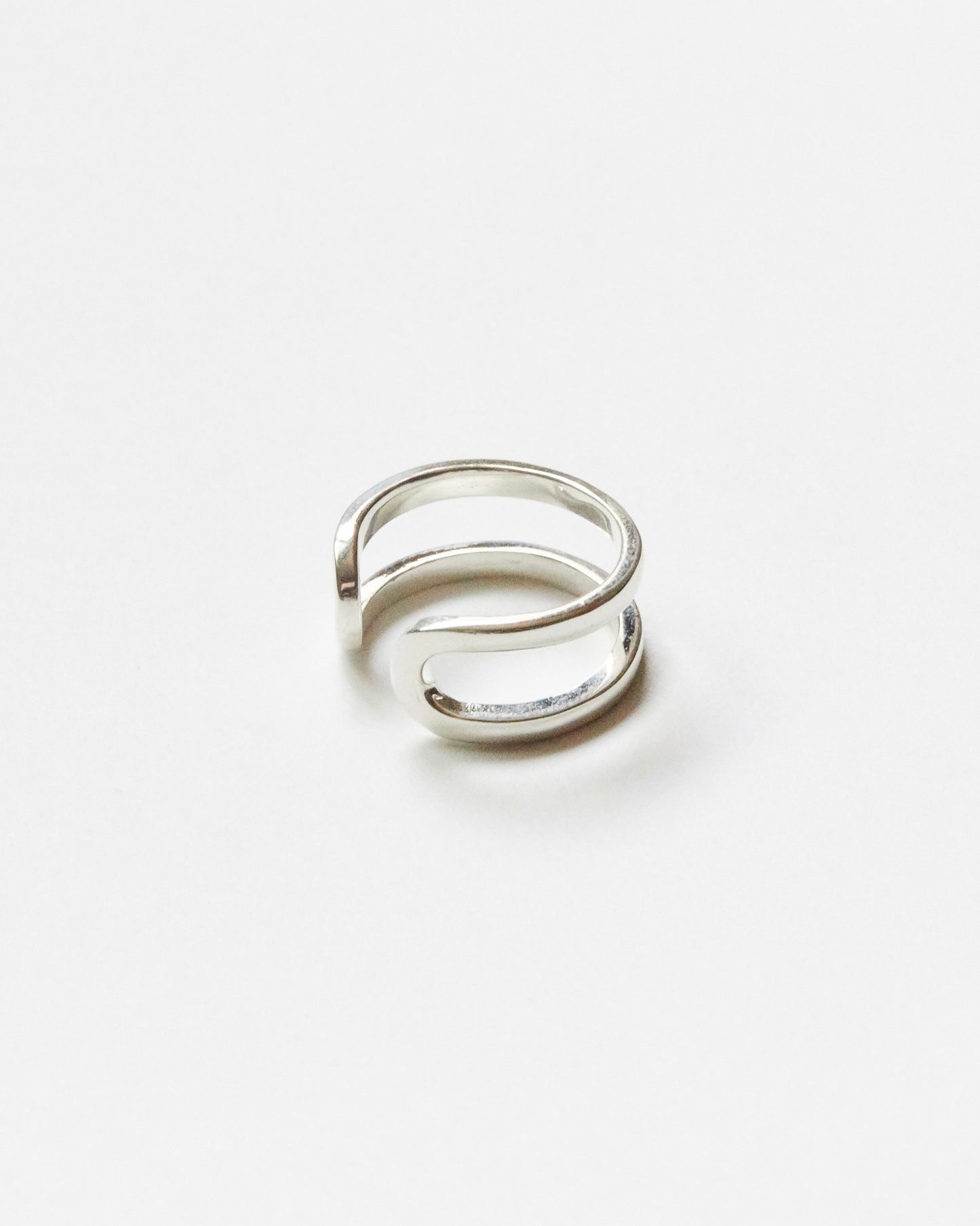 Close-up product image of a minimalist sterling silver open ring with double curved band design on clean white background, featuring sculptural contemporary silhouette.