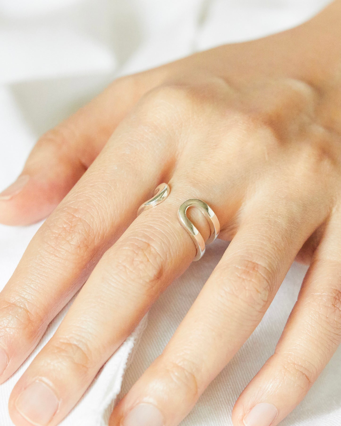 Minimal sterling silver open ring worn on finger featuring a sculptural double-line curved silhouette, styled on hand for an everyday modern jewelry look with clean minimal aesthetic.