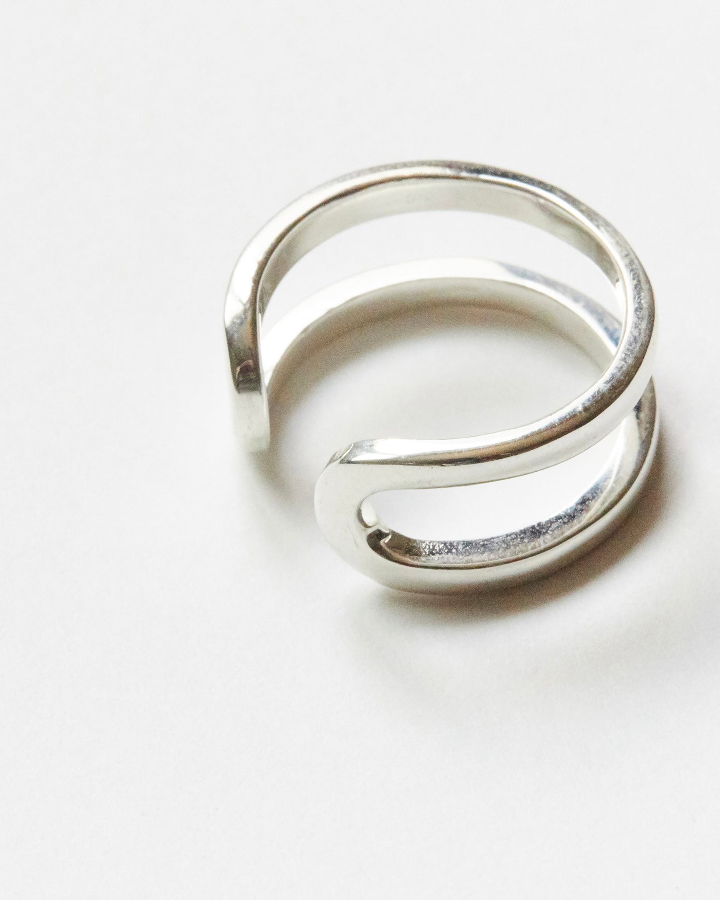 Macro close-up of a sterling silver open ring featuring fluid curved double bands and polished handcrafted finish on white background.
