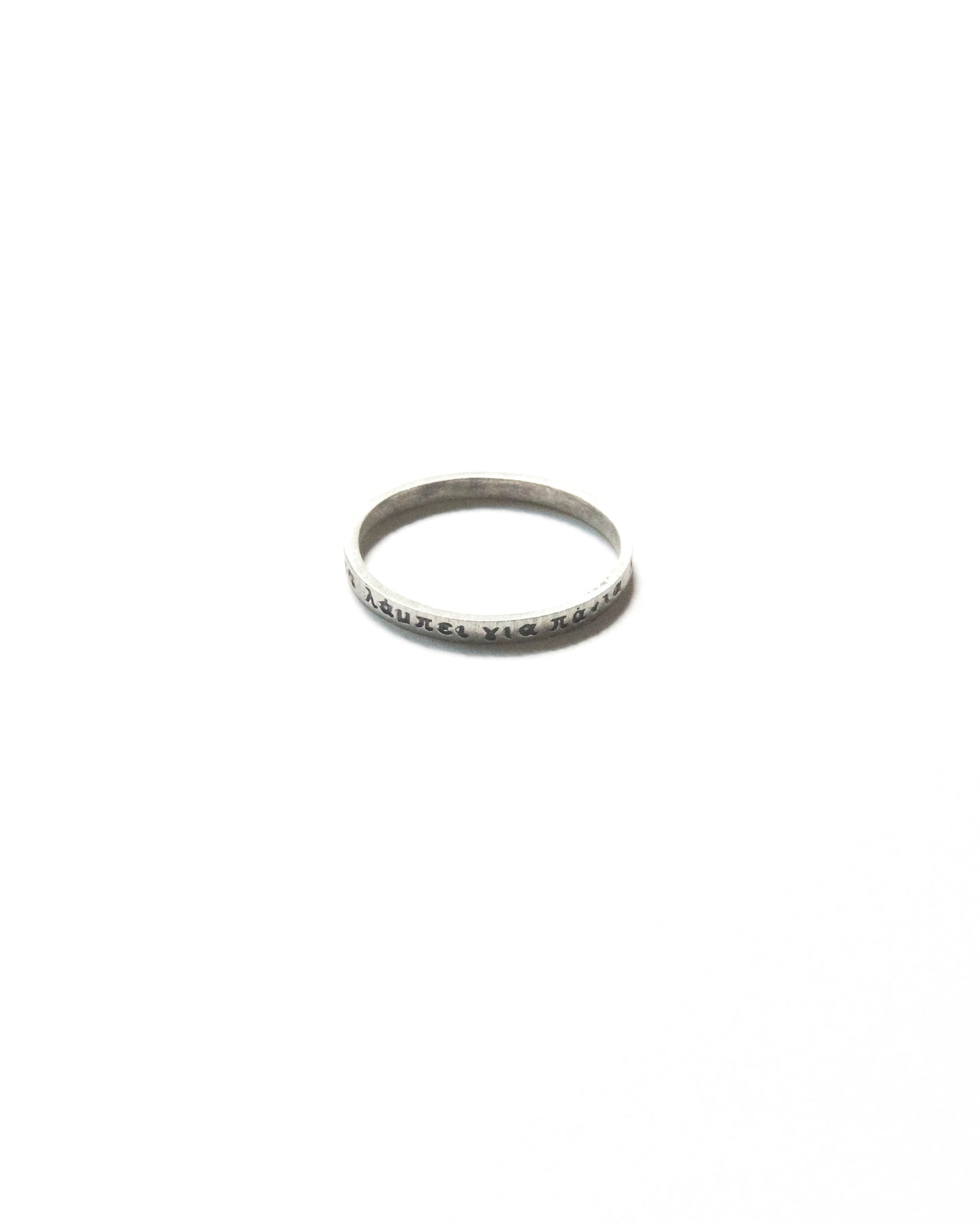 Close-up of a thin silver ring engraved with Greek text, photographed on a white background