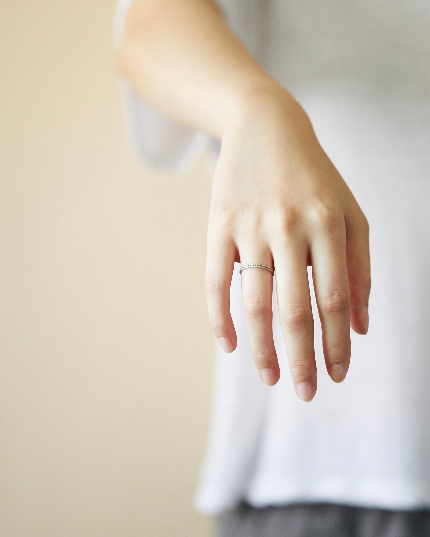 Slim silver ring worn on middle finger, paired with a white cotton top, showcasing casual styling