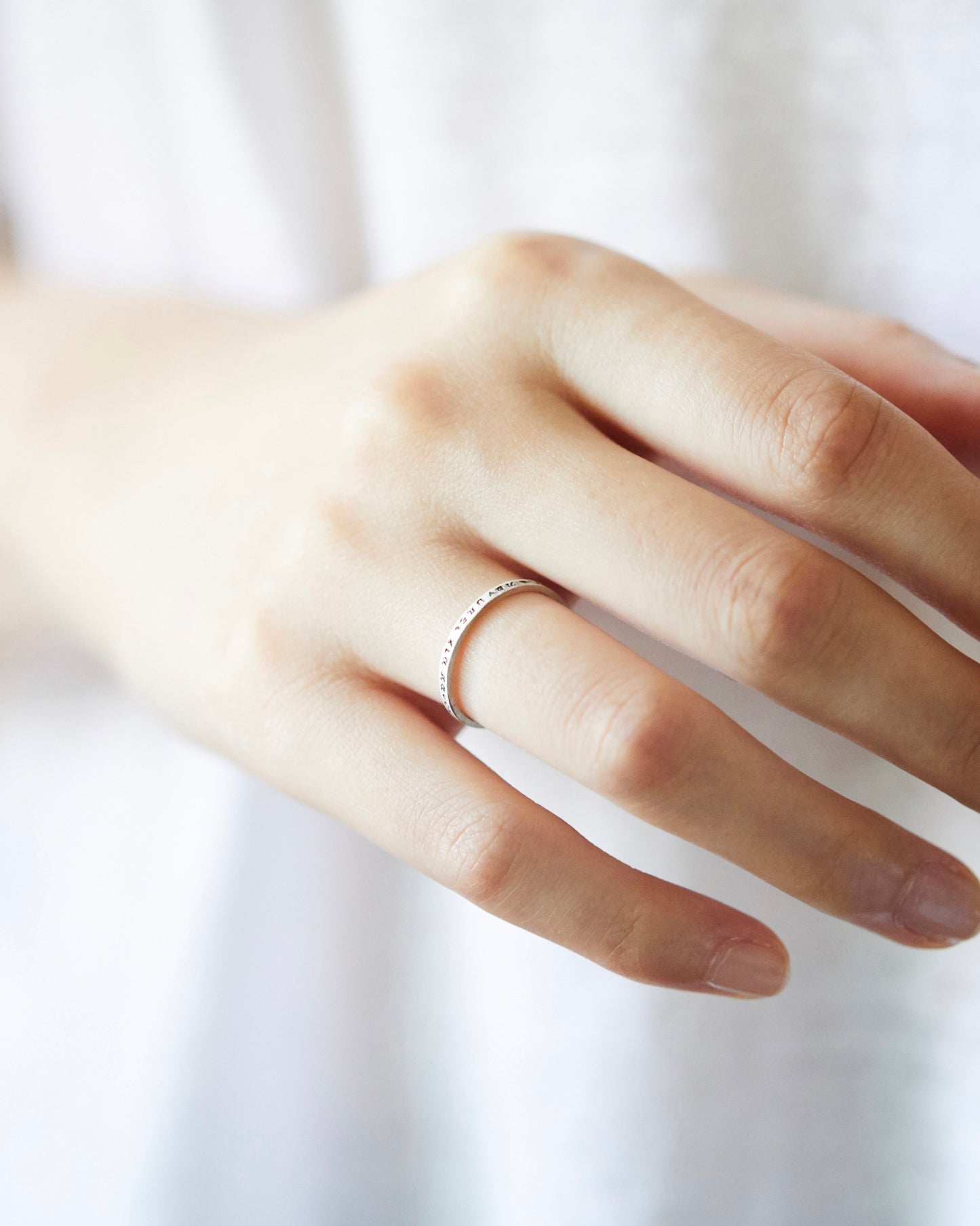 Model resting hand on shoulder, wearing slim engraved ring in a soft, natural setting