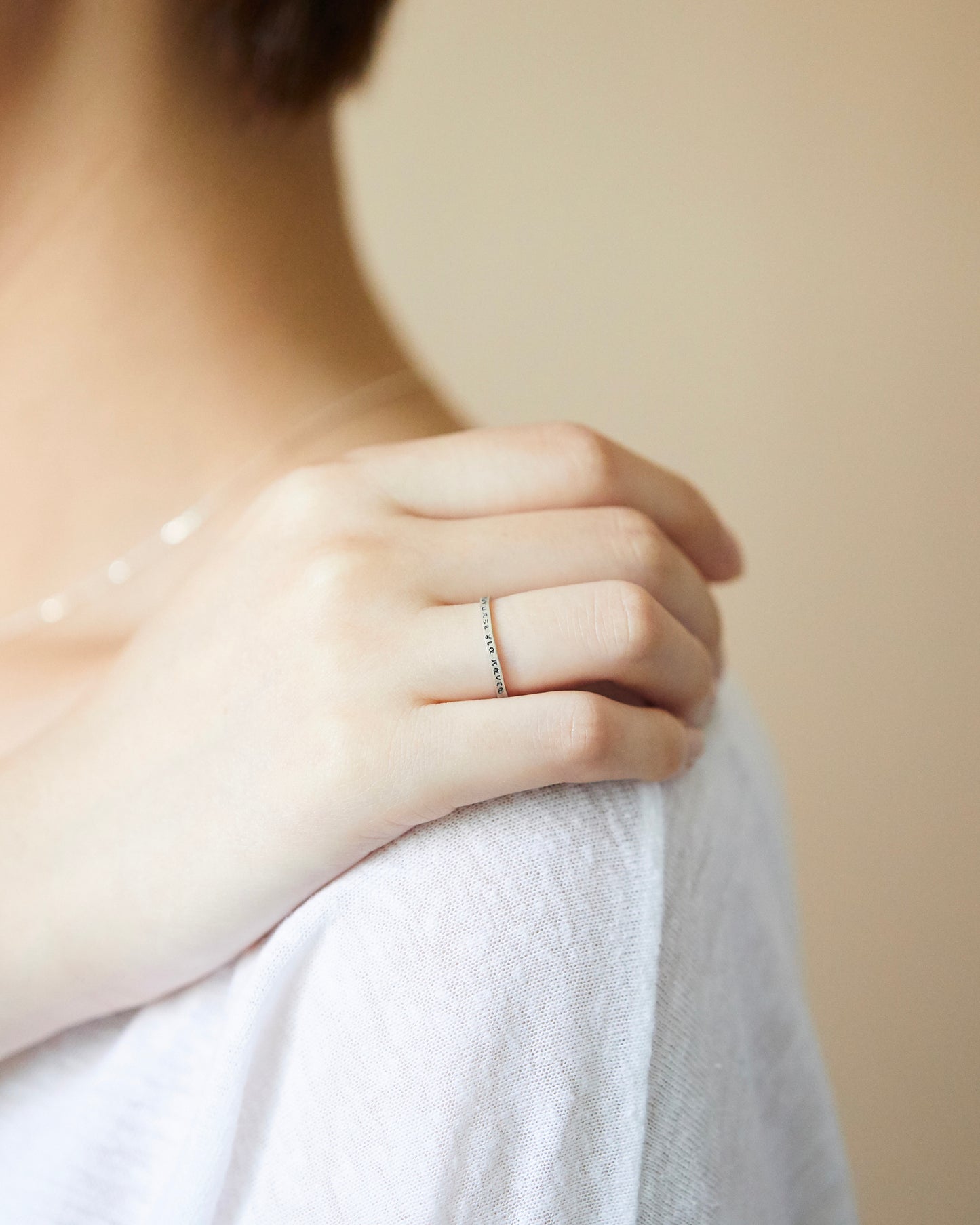 Model hand extended downward, wearing slim engraved silver band, styled with a loose-fit top