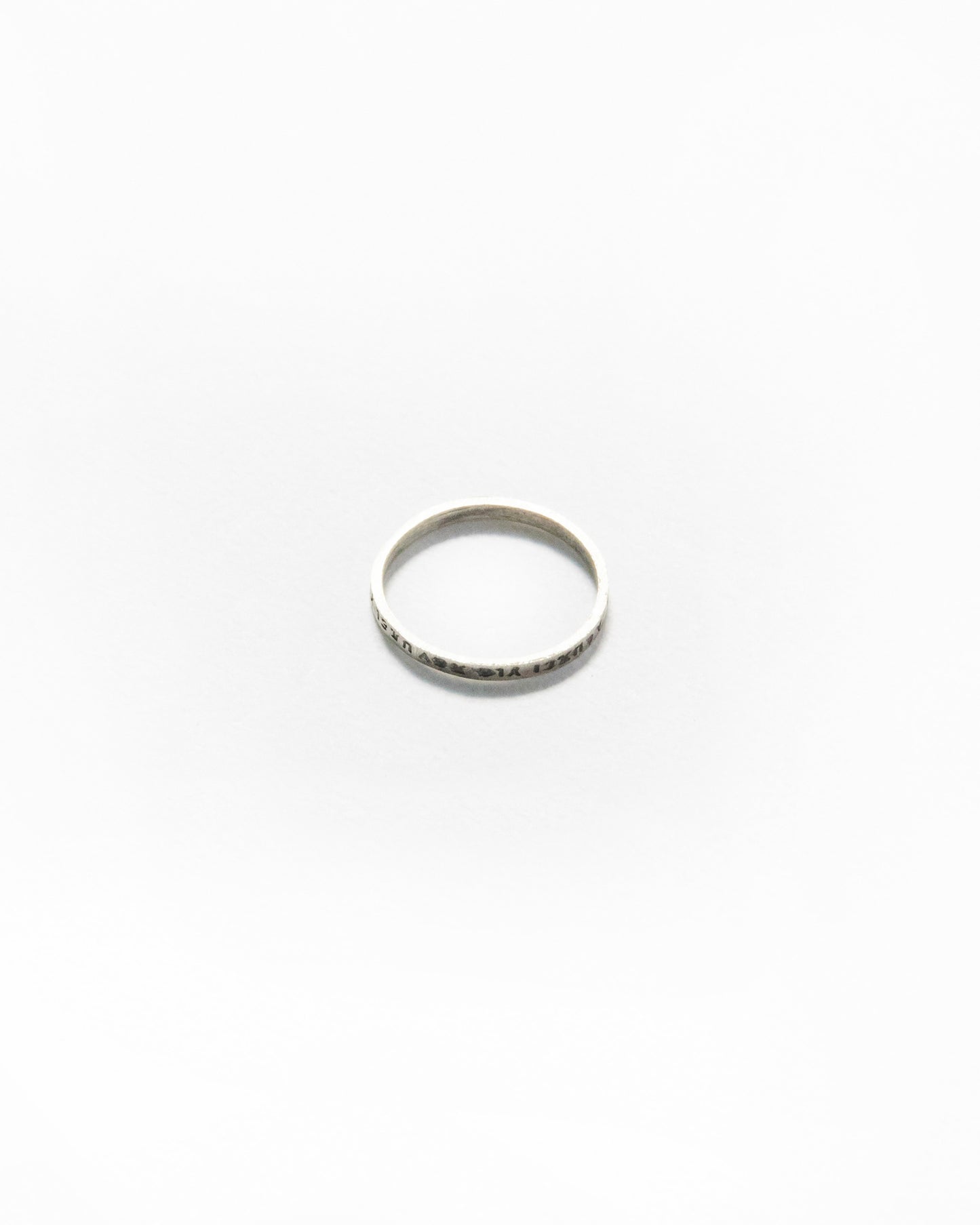 Top-view of slim engraved ring placed on white background, slightly oxidized finish for contrast