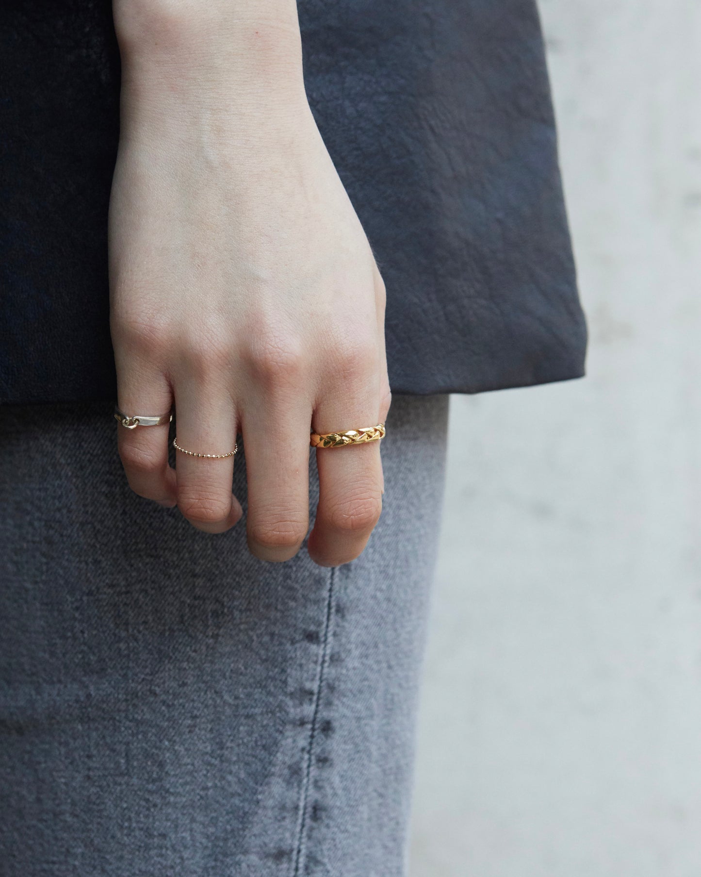 Gold braided ring styled solo on finger, creating a clean and warm contrast against a dark outfit