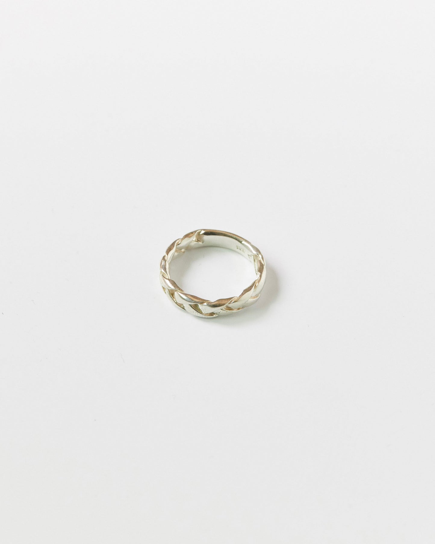 Close-up of a silver braided ring resting on a white background, showcasing its twisted woven design