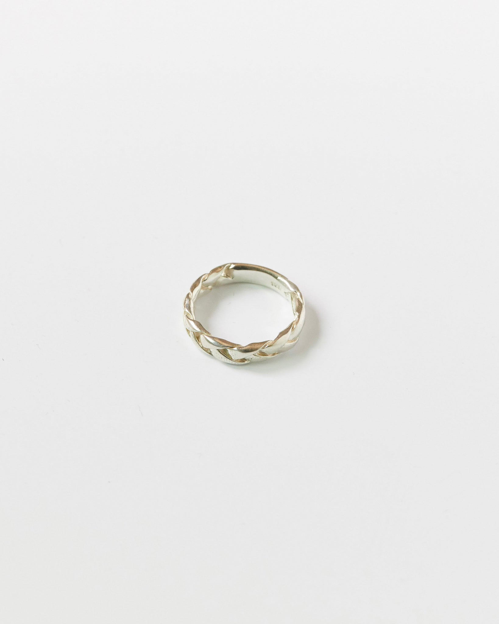 Close-up of a silver braided ring resting on a white background, showcasing its twisted woven design