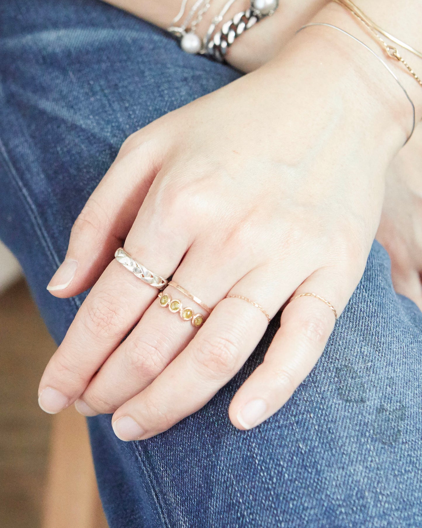 Braided silver ring worn on index finger, styled with a bold rectangular statement ring and thin gold bands