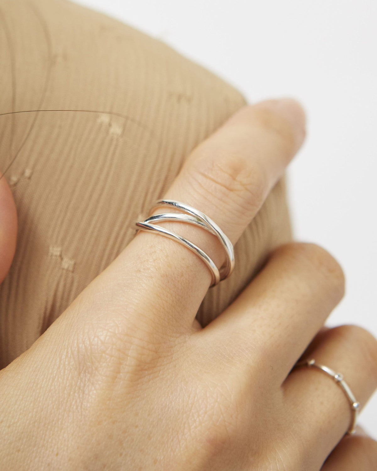 Silver triple line ring worn on the index finger against a beige knit – HANNA543 R506 triple air lines