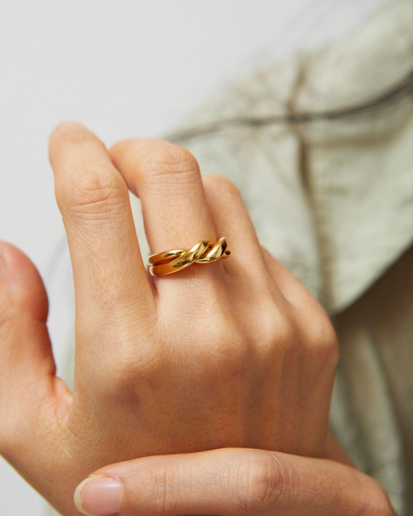 Twisted gold ring worn by model with raised fingers, against blurred background