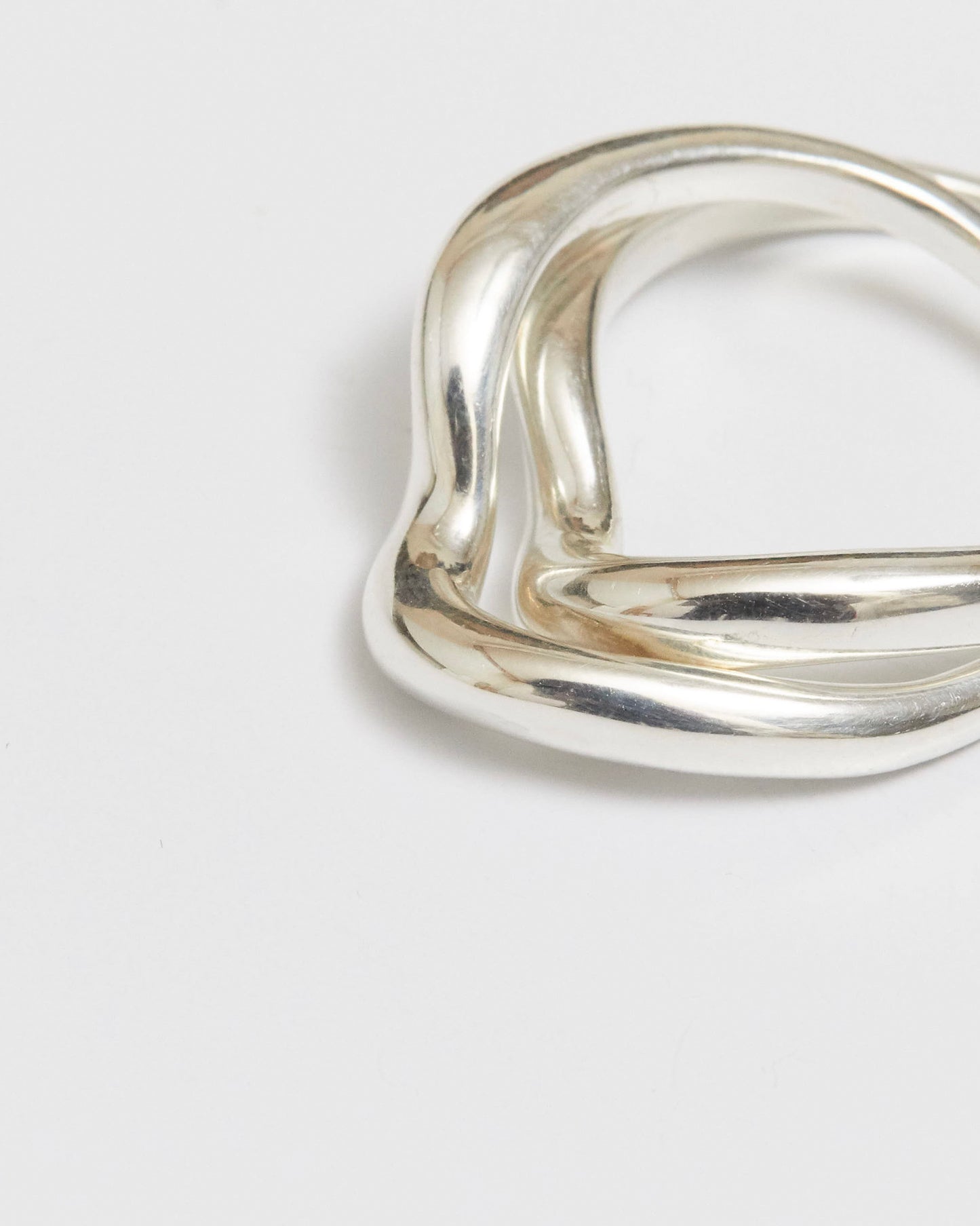 Close-up of thick silver rings with wave-like contours, overlapping on white