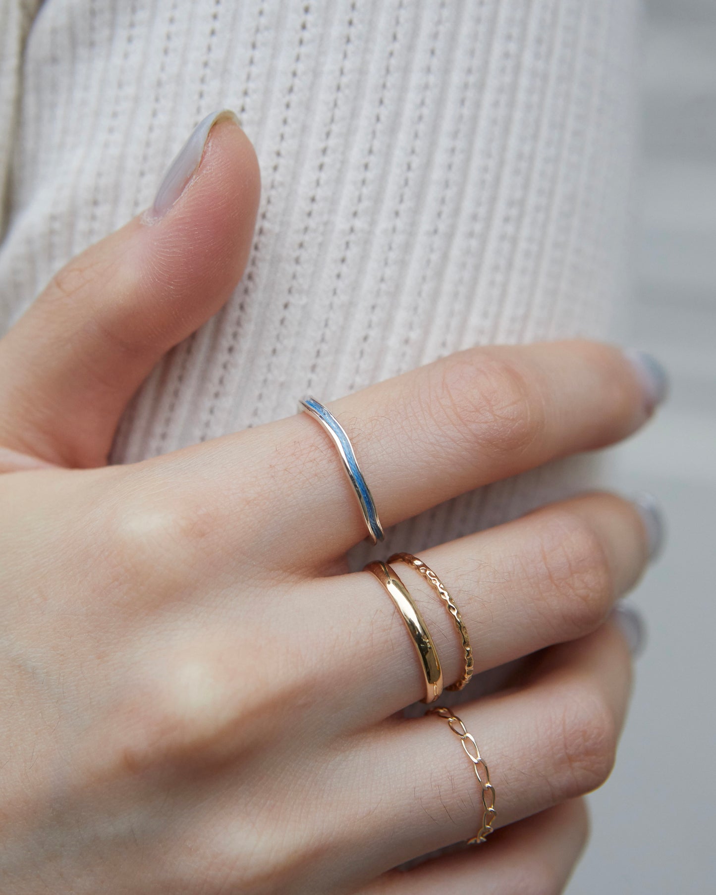A sky-blue minimalist ring worn on the index finger alongside a sculptural open ring.
