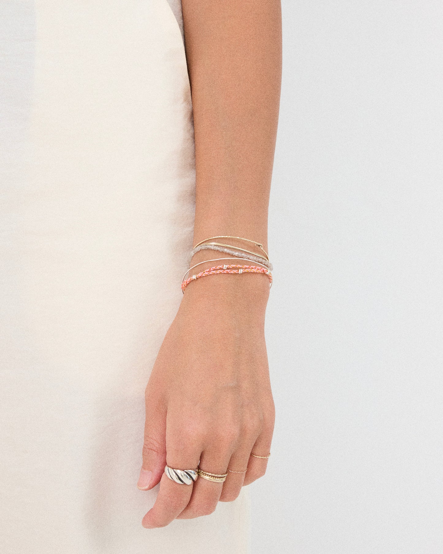 Pink braided bracelet layered with silver bangles on wrist