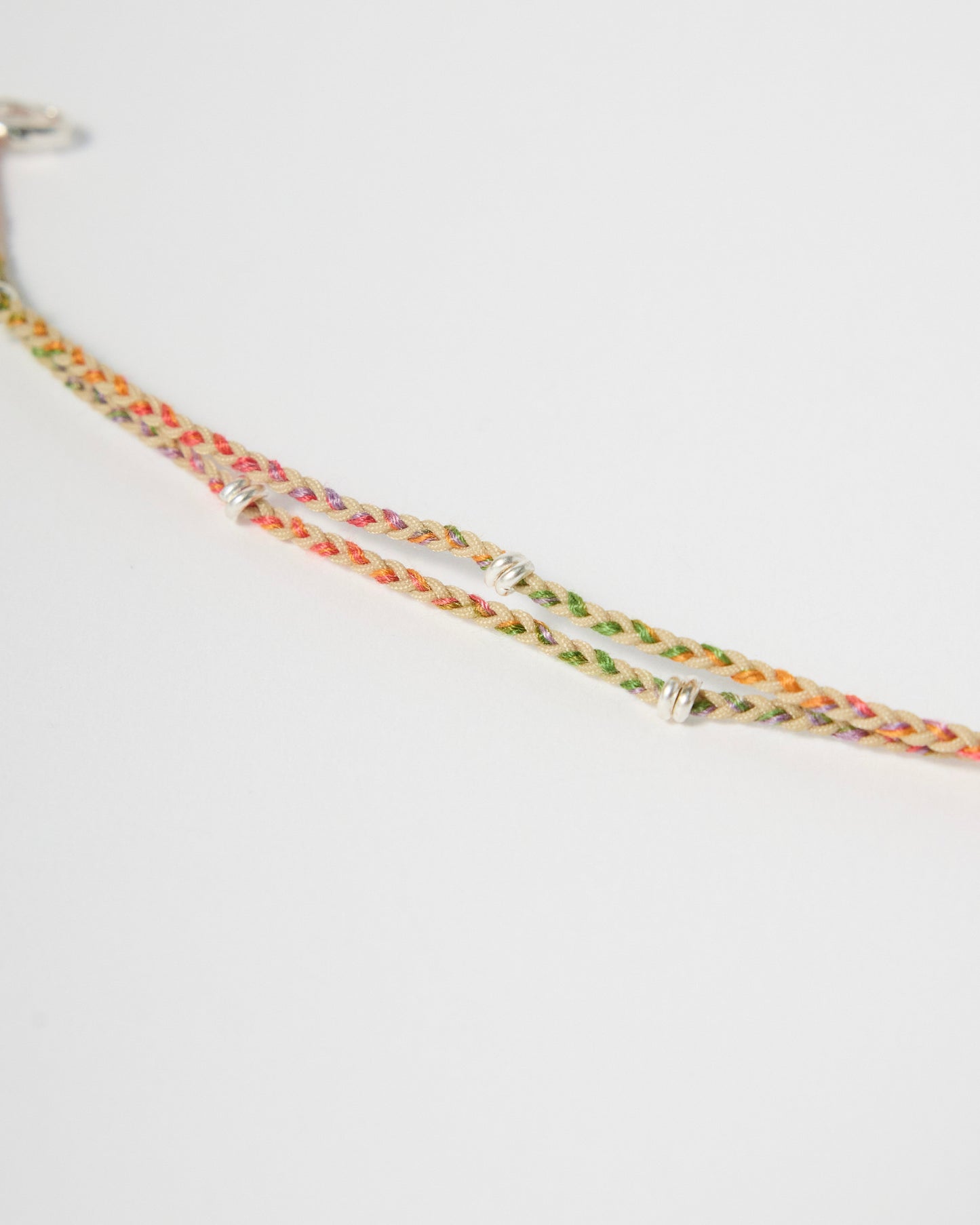 Close-up of handmade braided bracelet featuring pastel rainbow threads and sterling silver wraps