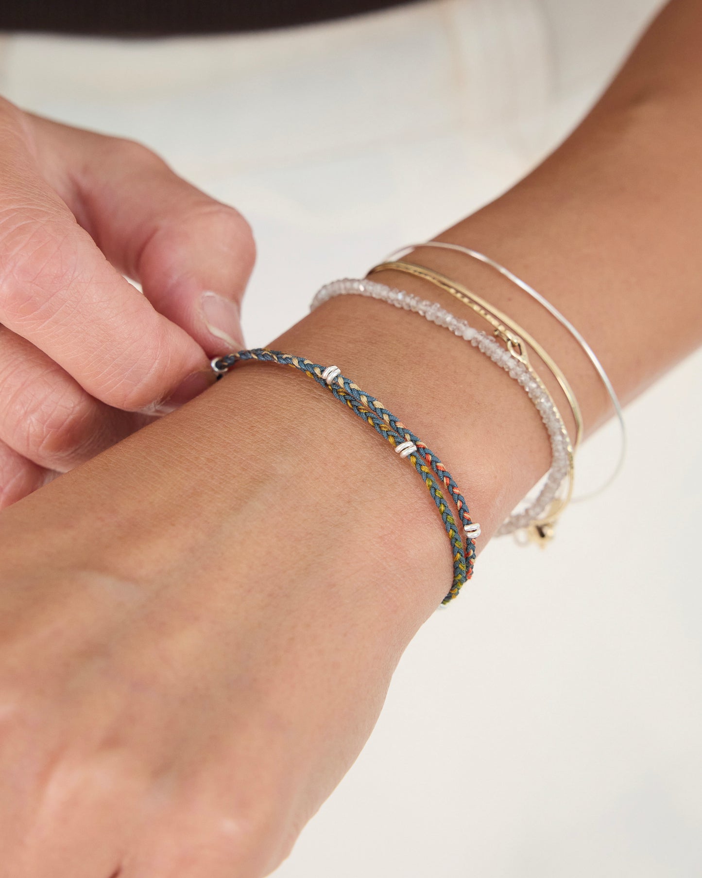 Close-up of handwoven earth-tone bracelet paired with layered gold and silver jewelry on wrist