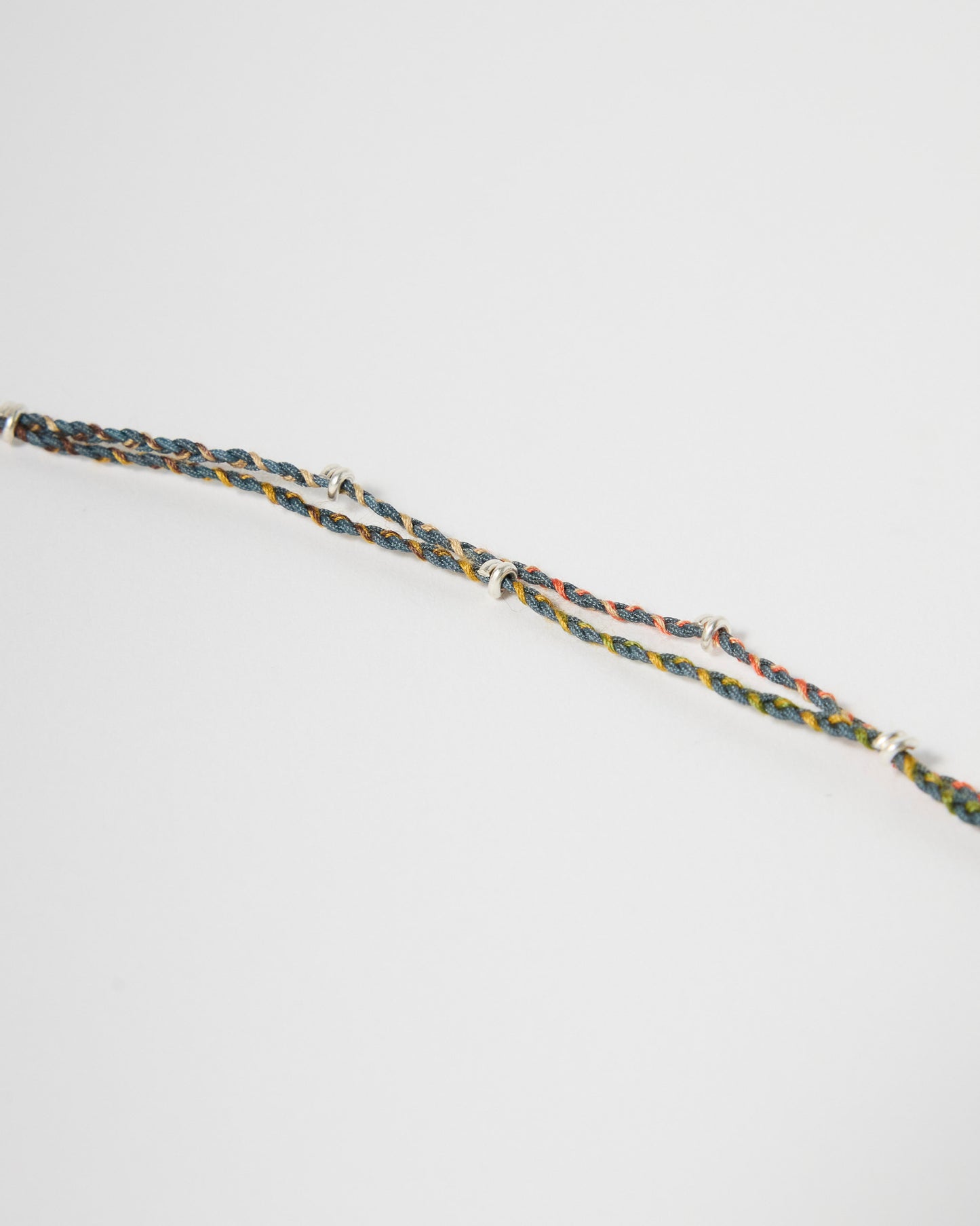 Close-up detail of braided cord bracelet with sterling silver wraps and multicolor woven threads
