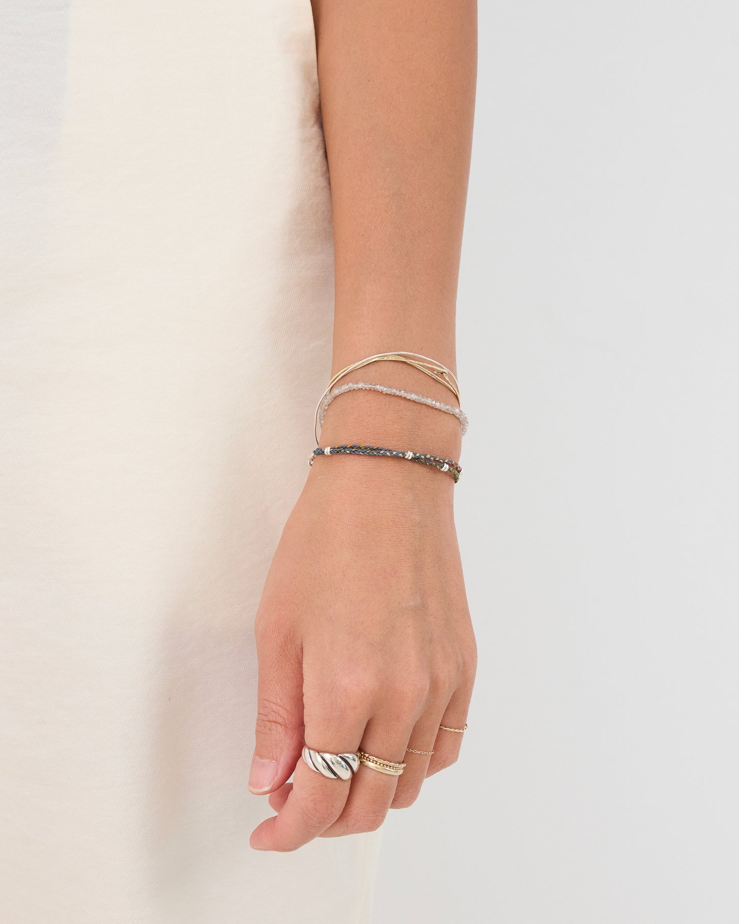 Minimalist woven bracelet styled with fine jewelry rings and layered bracelets for casual everyday wear