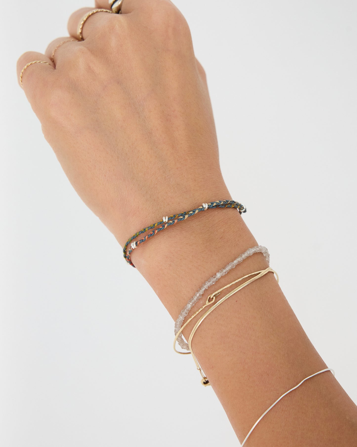Earth-tone braided bracelet layered with gold and silver bracelets for an everyday stacked jewelry look