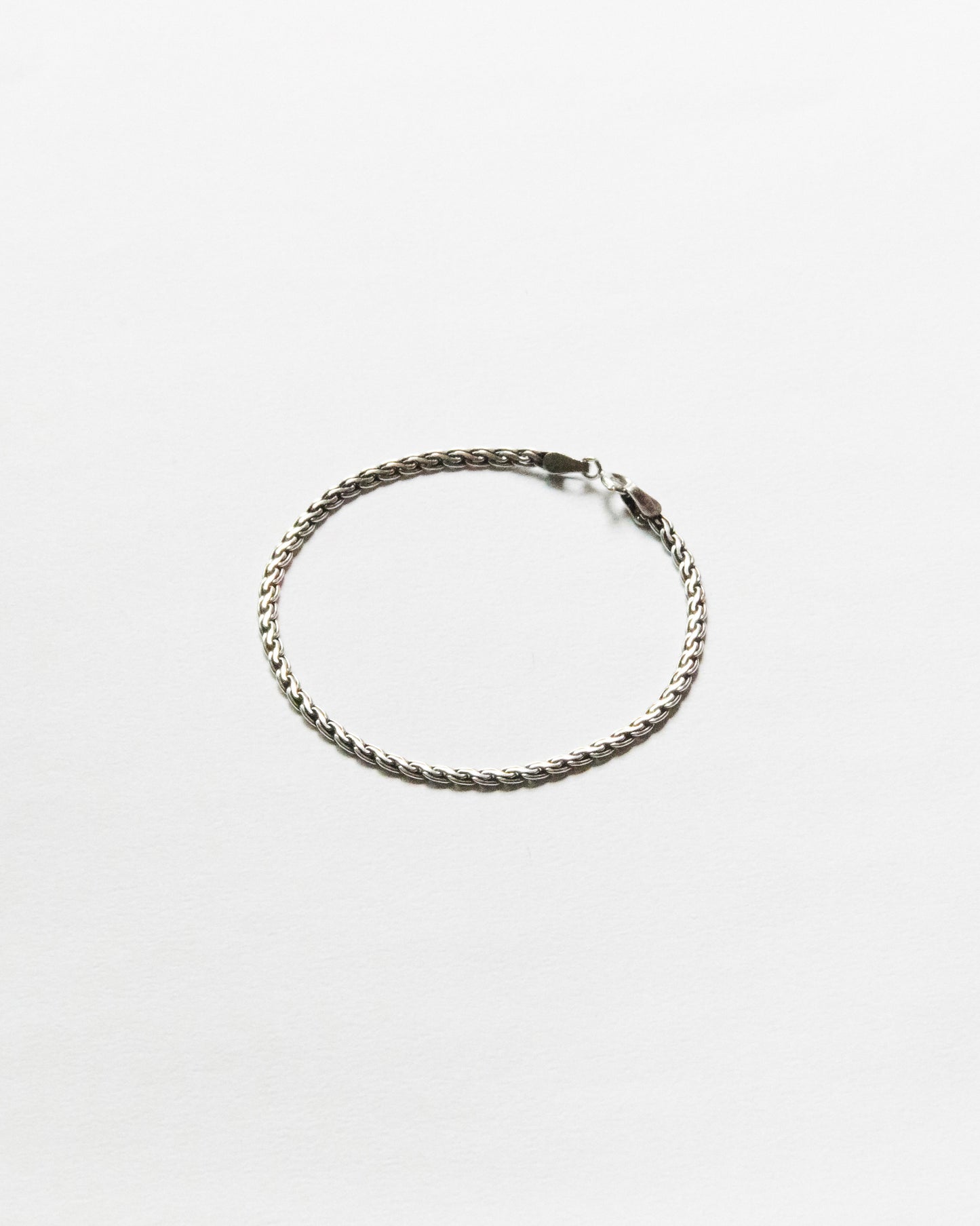Minimal woven sterling silver chain bracelet displayed on white background with polished finish and refined handcrafted texture.