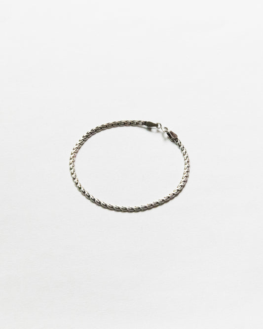 Minimal woven sterling silver chain bracelet displayed on white background with polished finish and refined handcrafted texture.