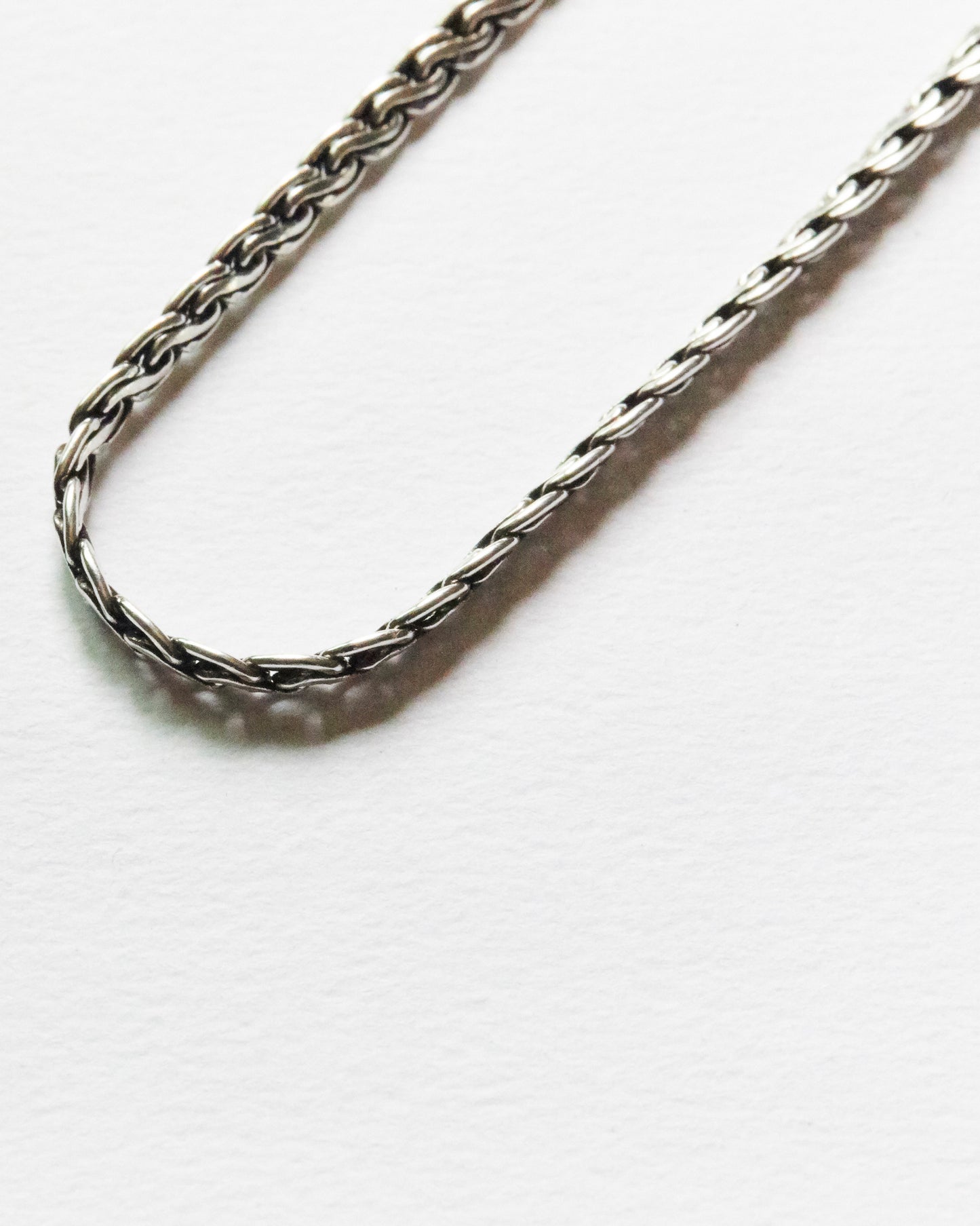 Close-up of minimalist sterling silver bracelet featuring intricate woven chain detail and polished finish on soft white background.