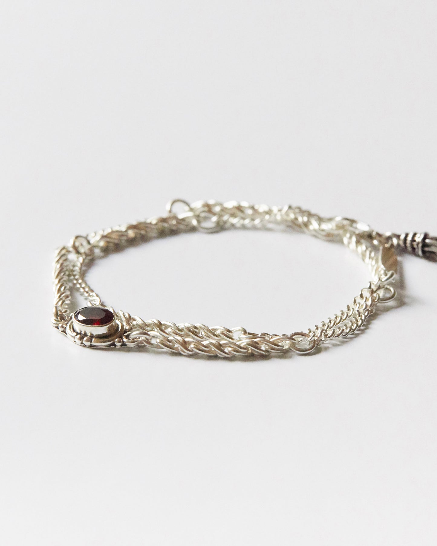 silver chain bracelet with twisted links and a single red gemstone detail laid flat