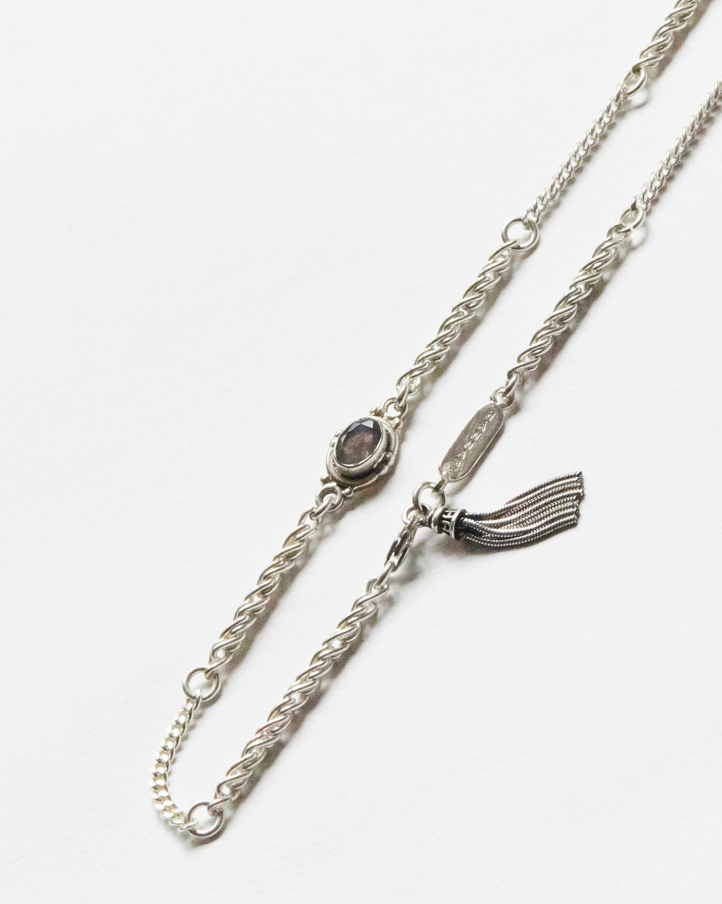 silver chain bracelet with twisted links and a single grey gemstone detail laid flat