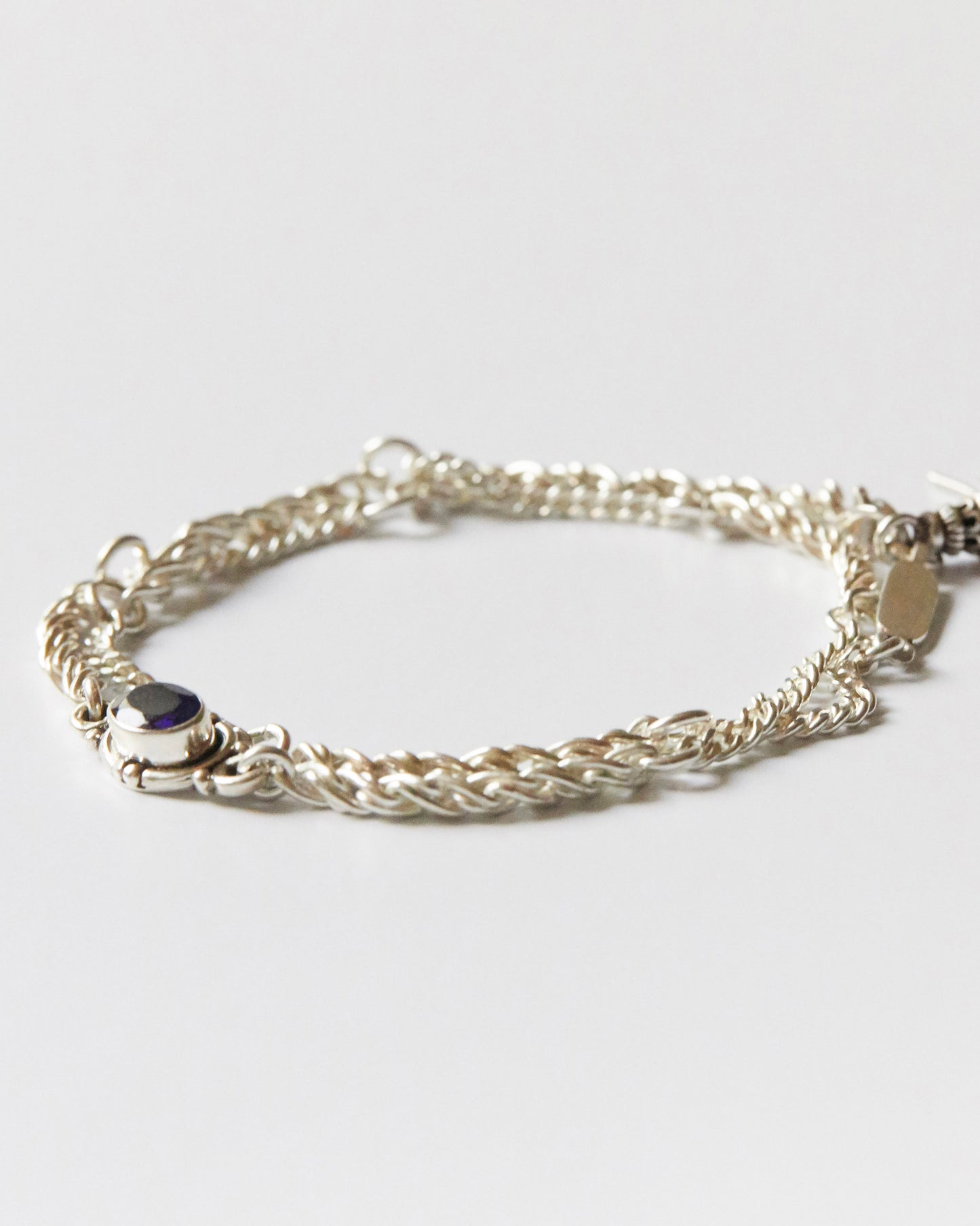 silver chain bracelet with twisted links and a single purple gemstone detail laid flat