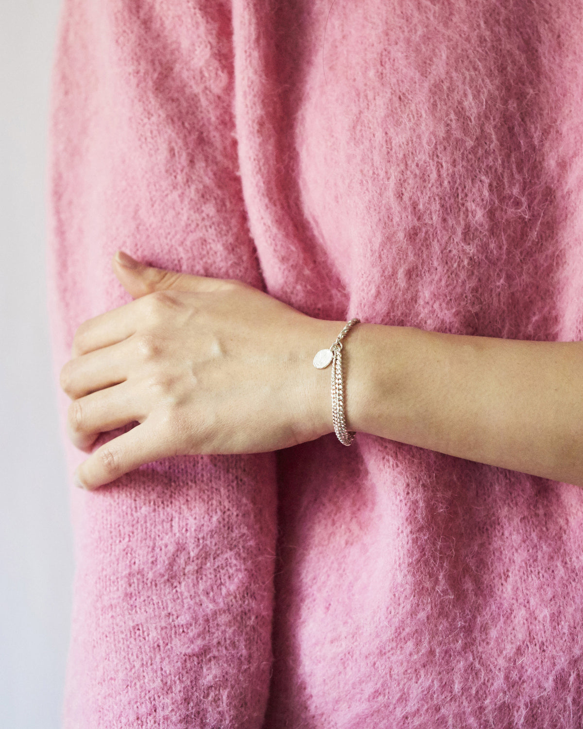 Hanna543 silver chain bracelet with a sculpted coin charm, paired with a soft pink knit for a delicate and contemporary look.