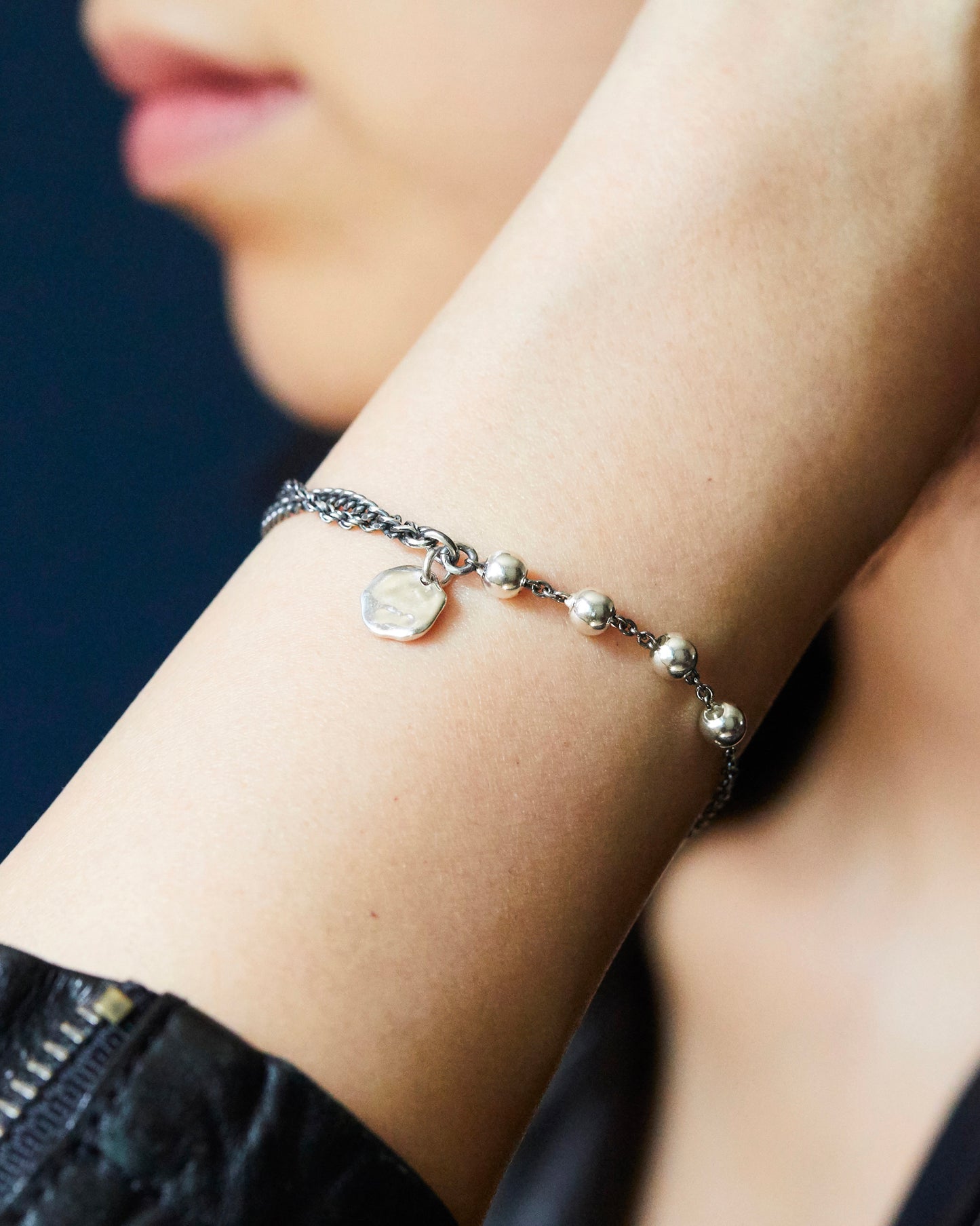 close-up of a wrist wearing a silver bracelet with beads against a dark background