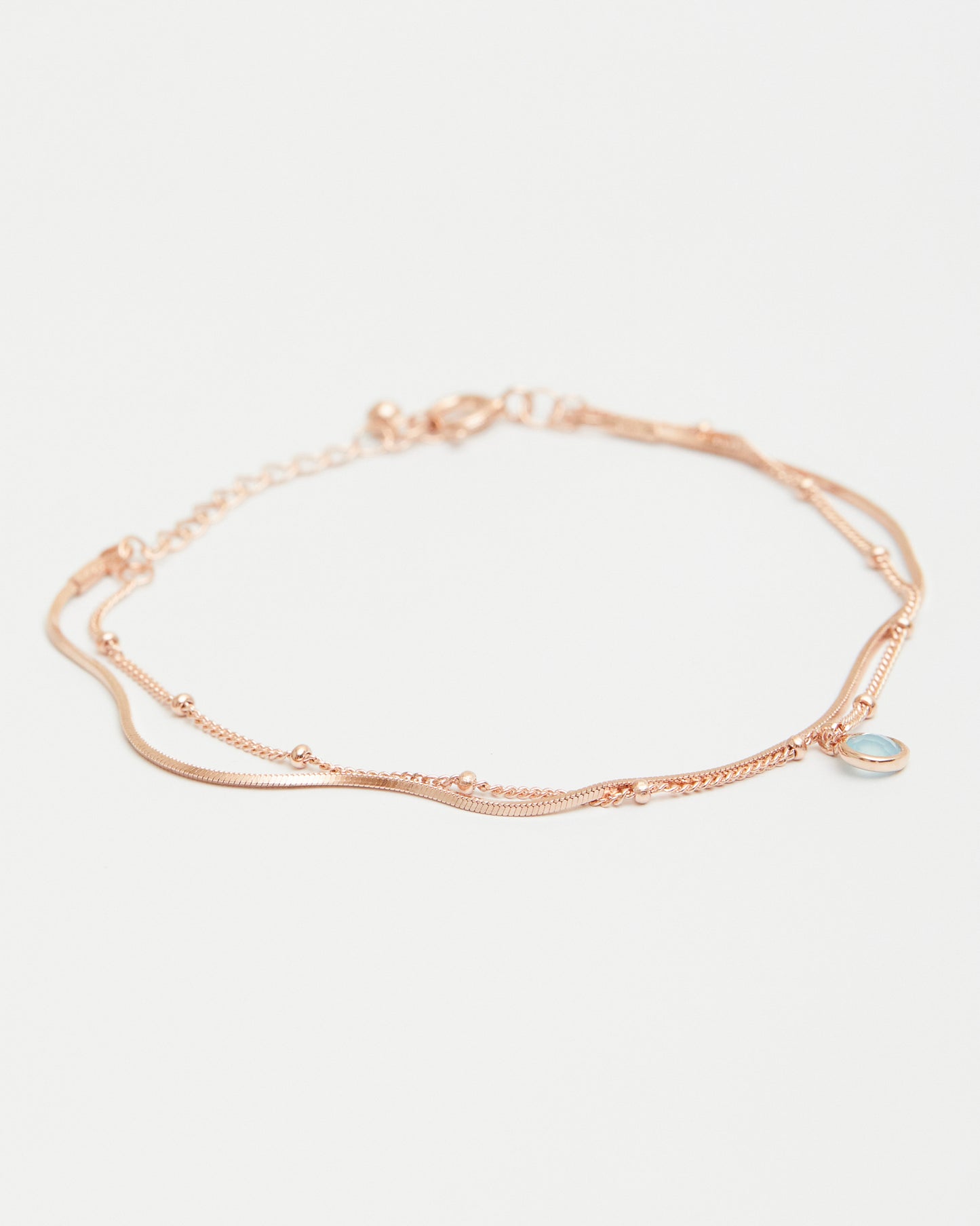 rose gold layered bracelet with blue gemstone charm on white background