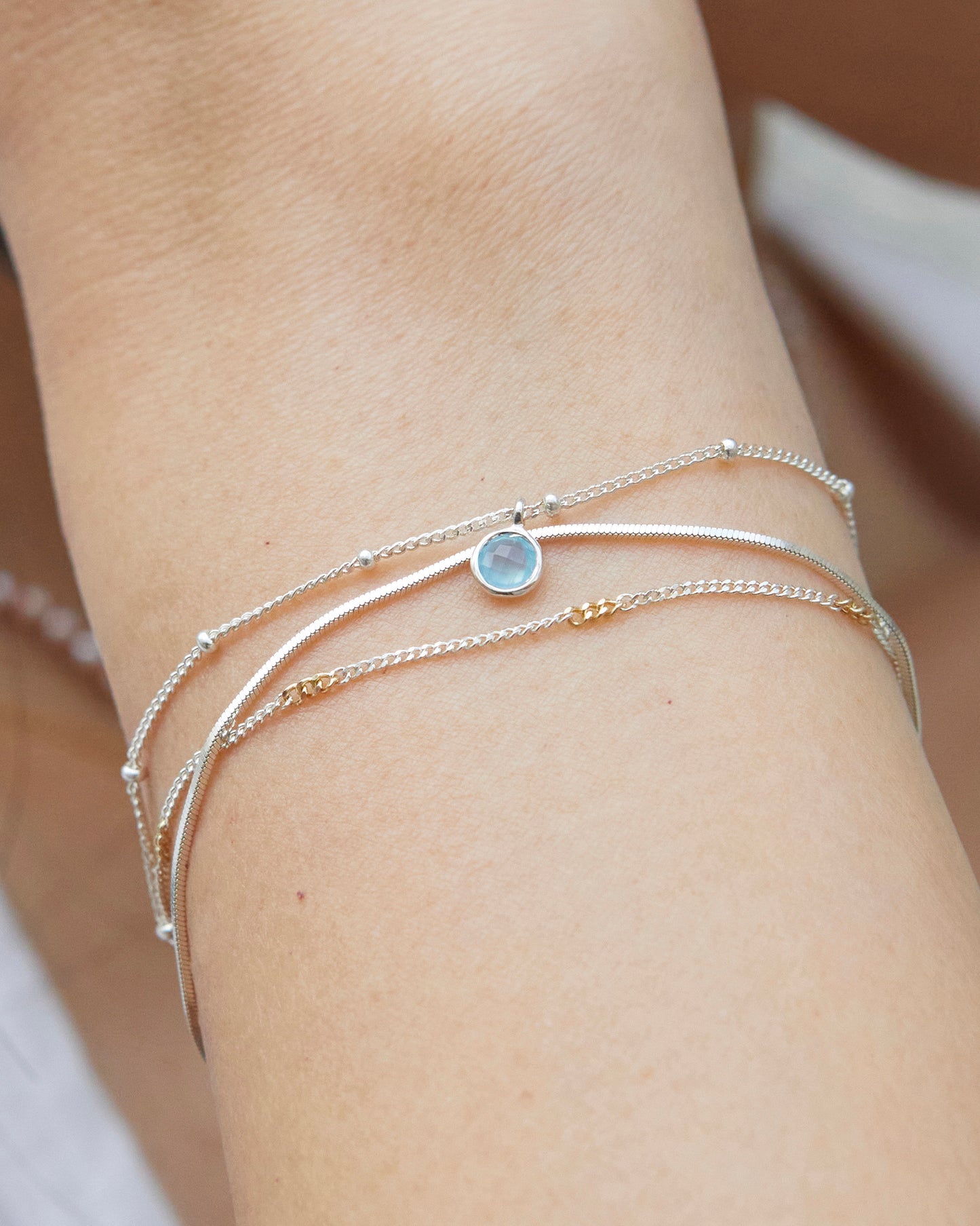 Layered sterling silver bracelet with blue charm worn on wrist