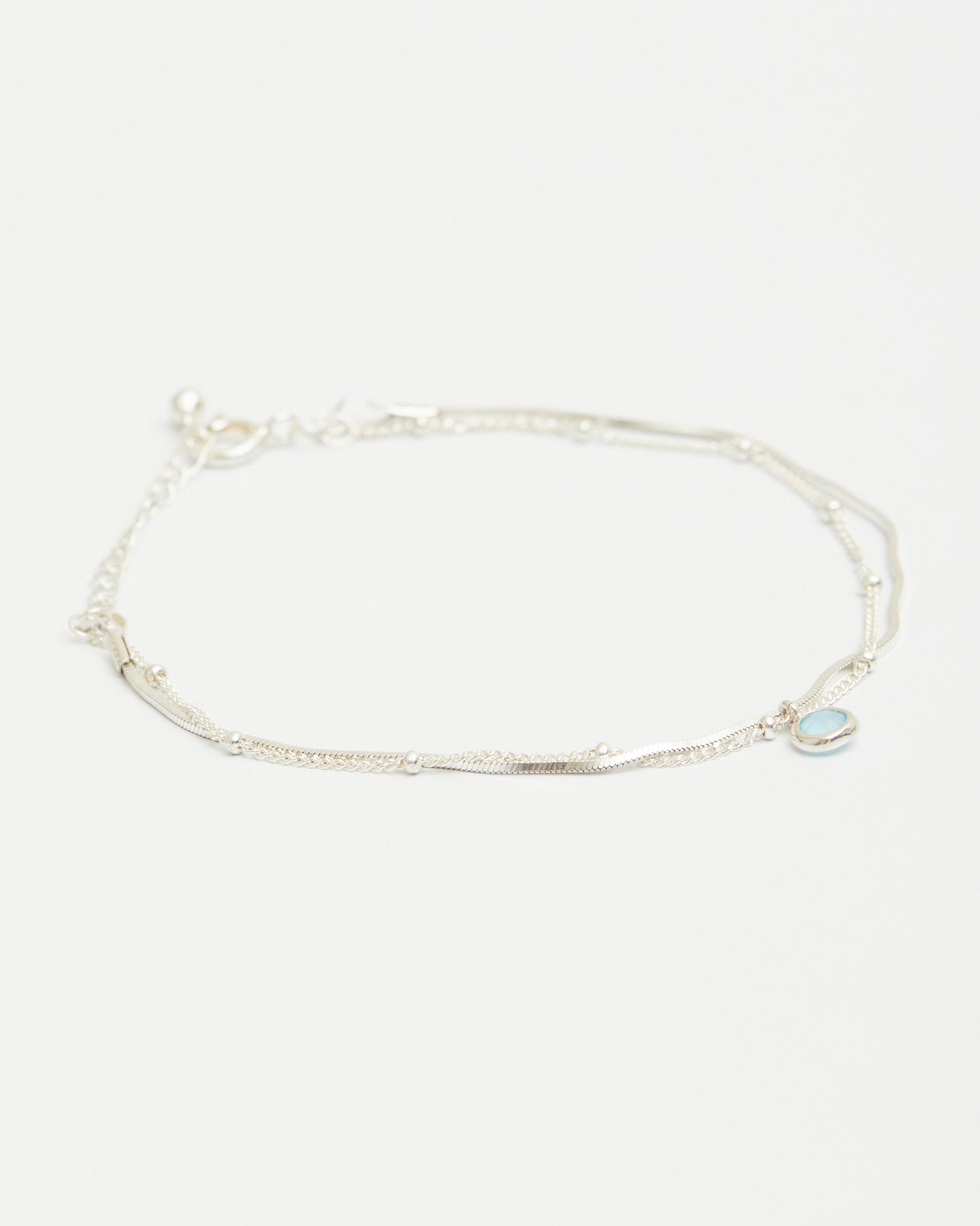 Sterling silver layered bracelet with blue gemstone charm on white background