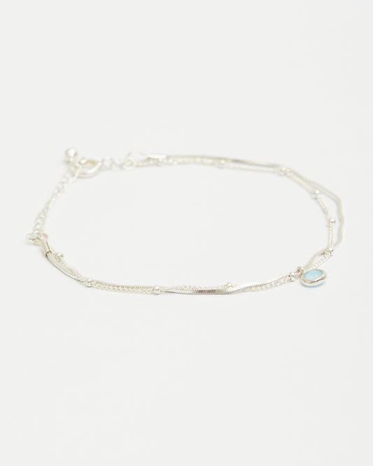 Sterling silver layered bracelet with blue gemstone charm on white background