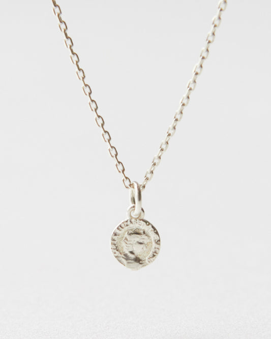 Close-up of a silver coin pendant necklace resting on white surface