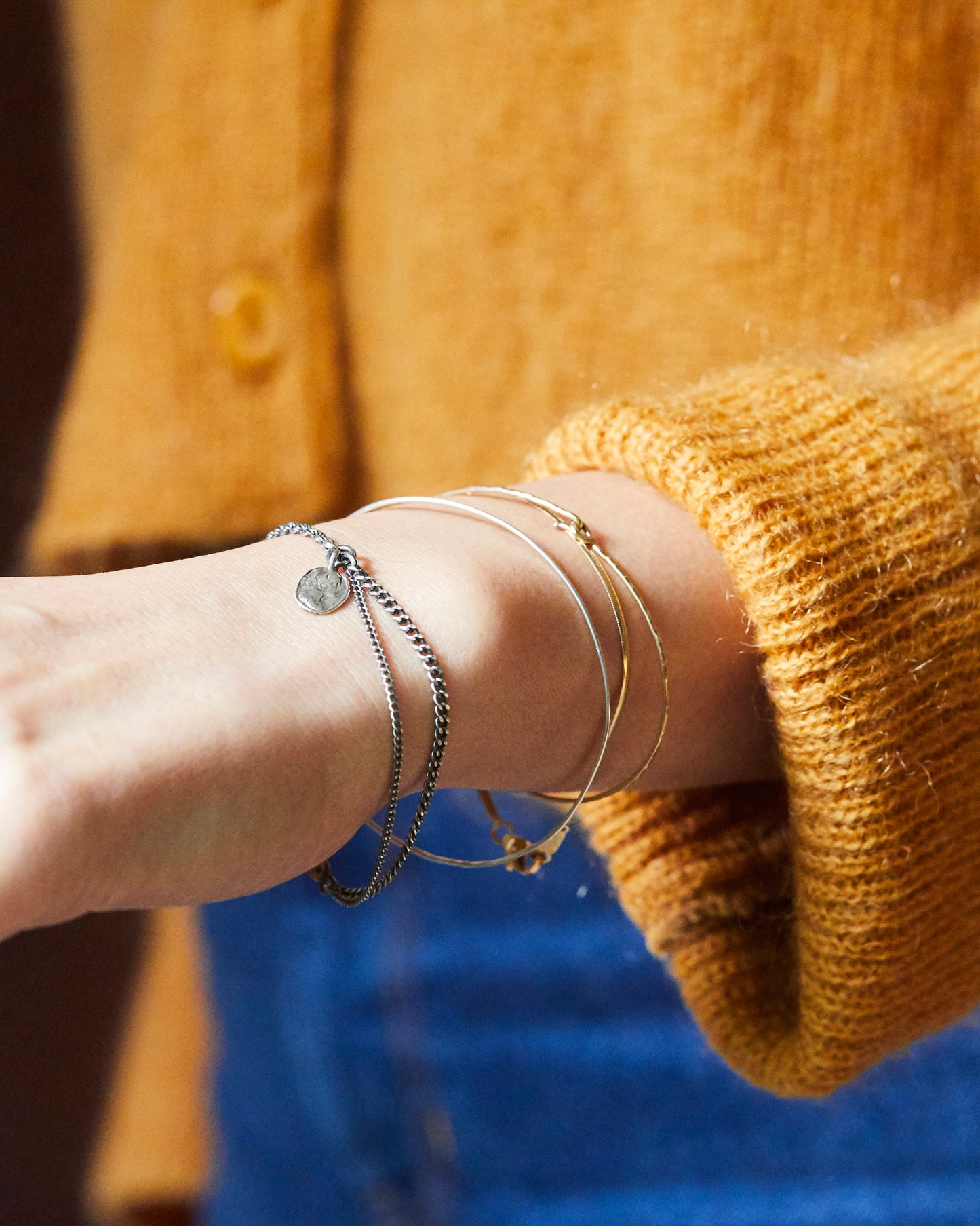 Minimalist silver bracelet with handcrafted coin charm, worn on wrist with layered bangles